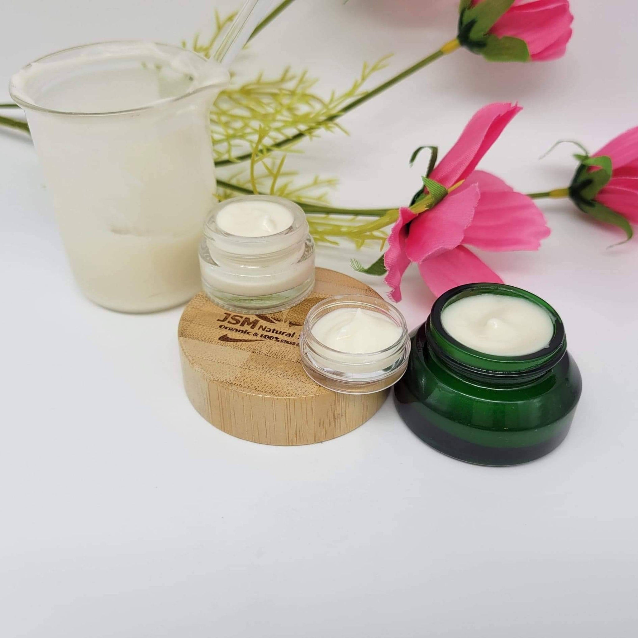 Cream jars with white cream, green and clear glass, and wooden base with JSM Natural logo visible
