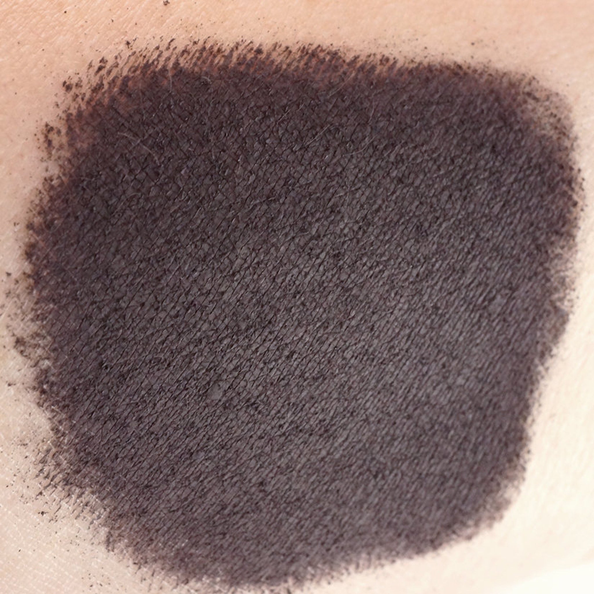 Close-up of matte dark purple loose mineral eyeshadow powder with rich aubergine pigment in a sifter jar