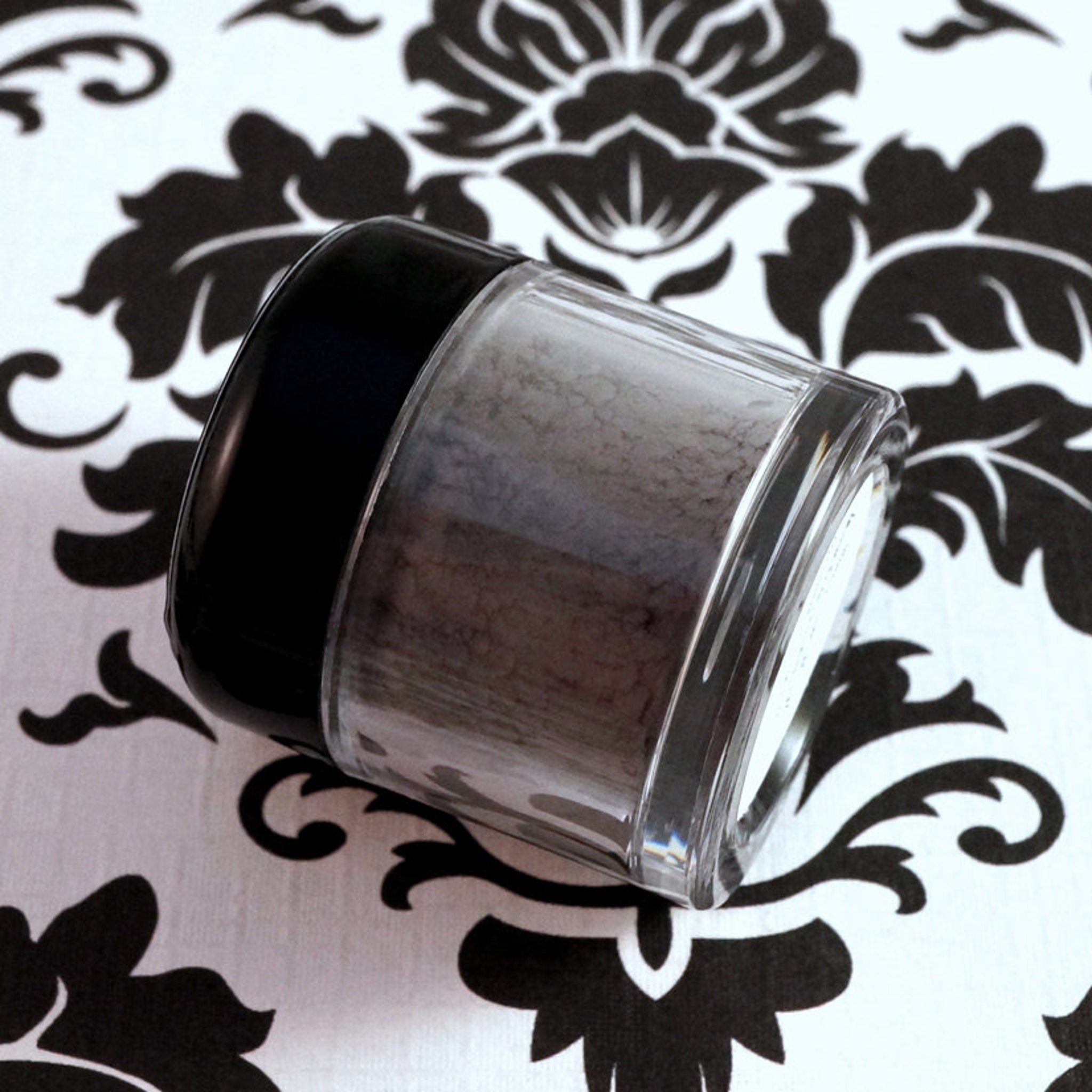 Close-up of matte dusty violet loose pigment eyeshadow in dark purple-gray shade with vegan label visible