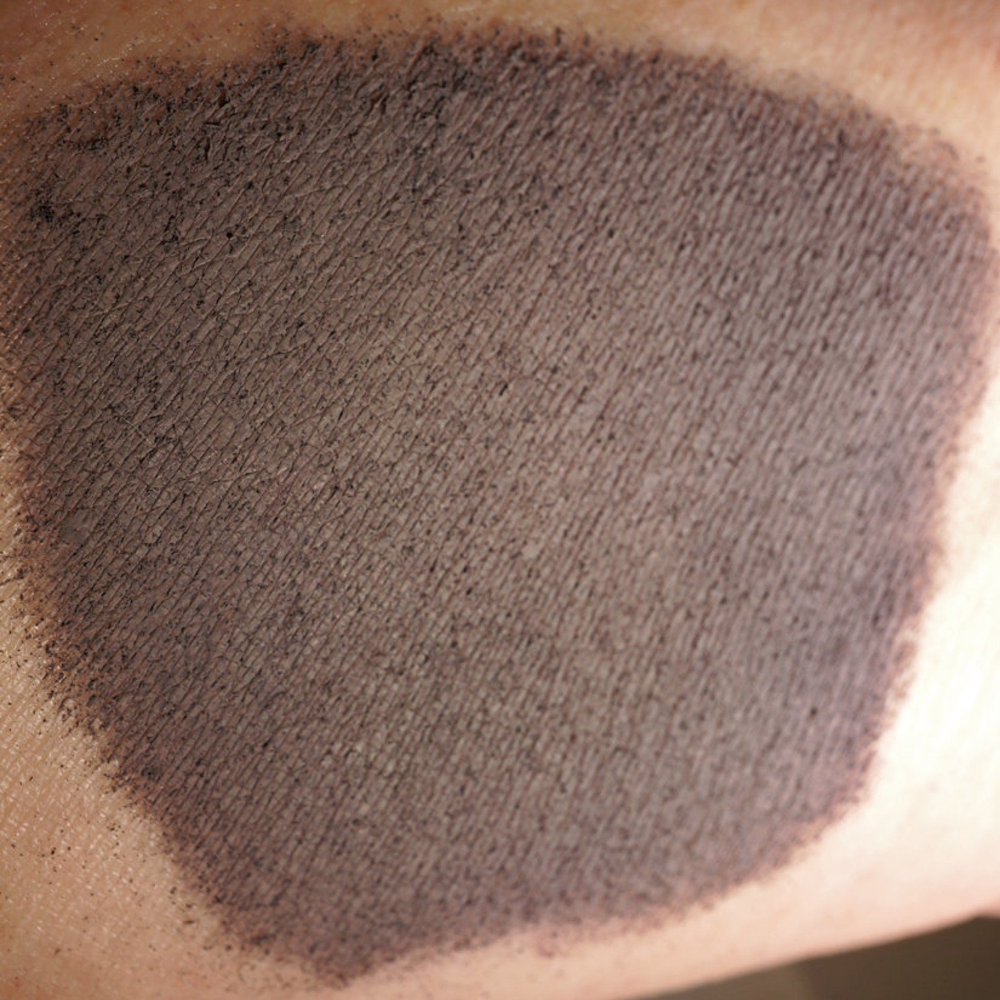 Side view of matte dusty violet loose pigment eyeshadow in dark purple-gray shade, showing fine powder texture