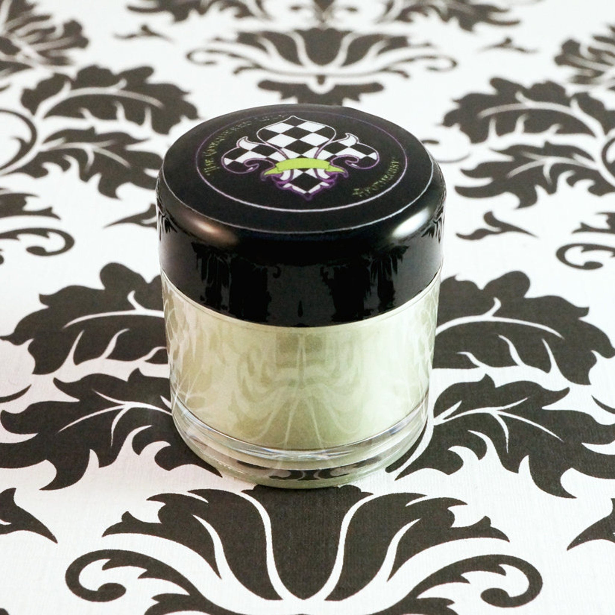 Side view of matte sage green loose mineral eyeshadow in glass jar with gold lid, showcasing fine powder texture