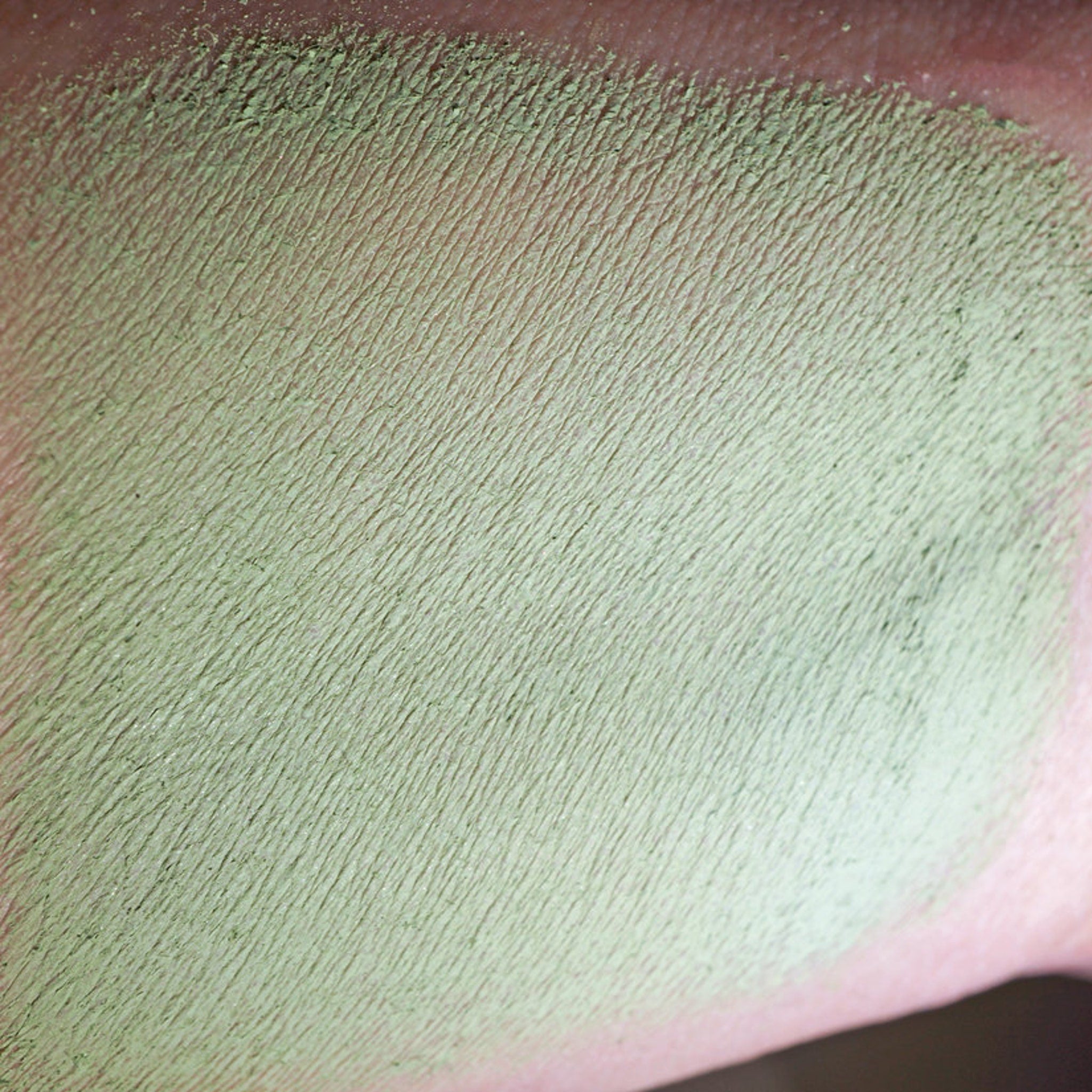 Side view of matte sage green loose mineral eyeshadow in a glass jar with black lid, showcasing olive undertones