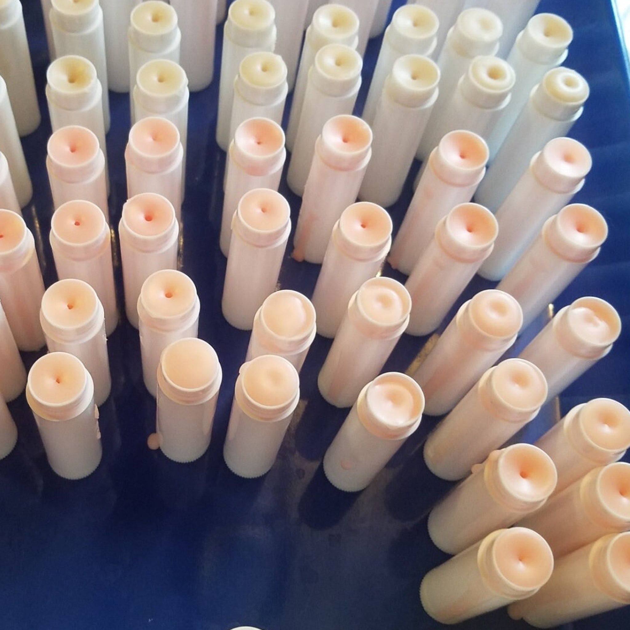 Lip balm tubes in white and peach with a cylindrical shape, arranged on a blue surface