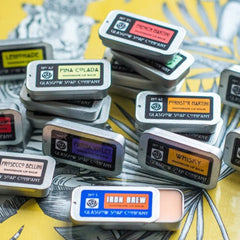 Lip balm tins with silver metal, colorful labels, and Glasgow Soap Company text on yellow background