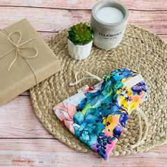 Floral print drawstring bag with blue, yellow, and pink colors, white drawstring, on woven mat