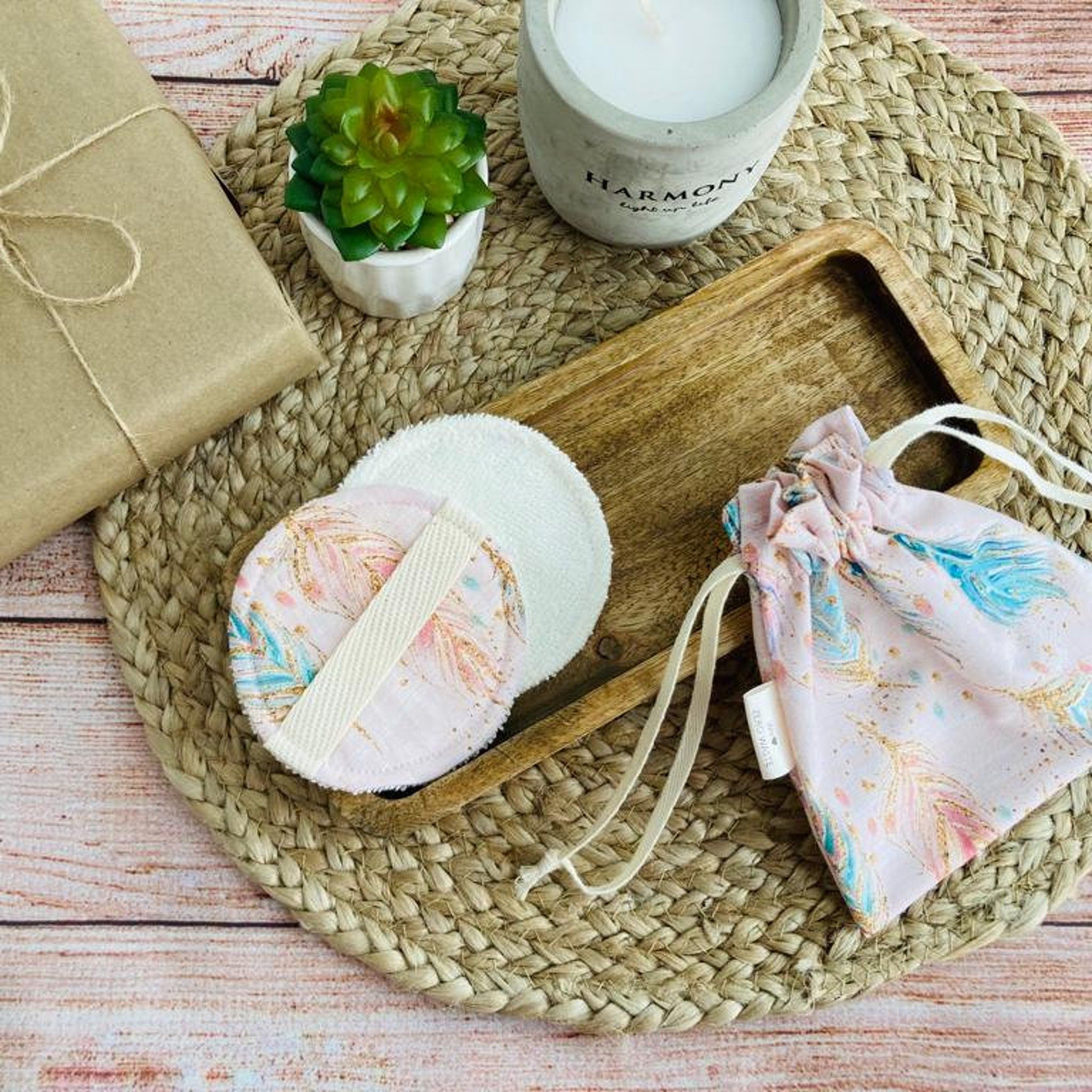 Reusable makeup pads with white, pink feather pattern, and drawstring bag on woven mat