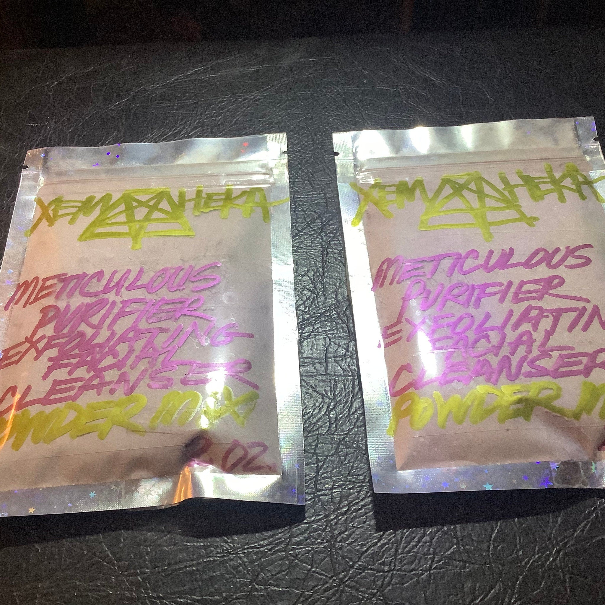 Facial cleanser powder packets, clear foil pouches, neon green and pink text, on black surface