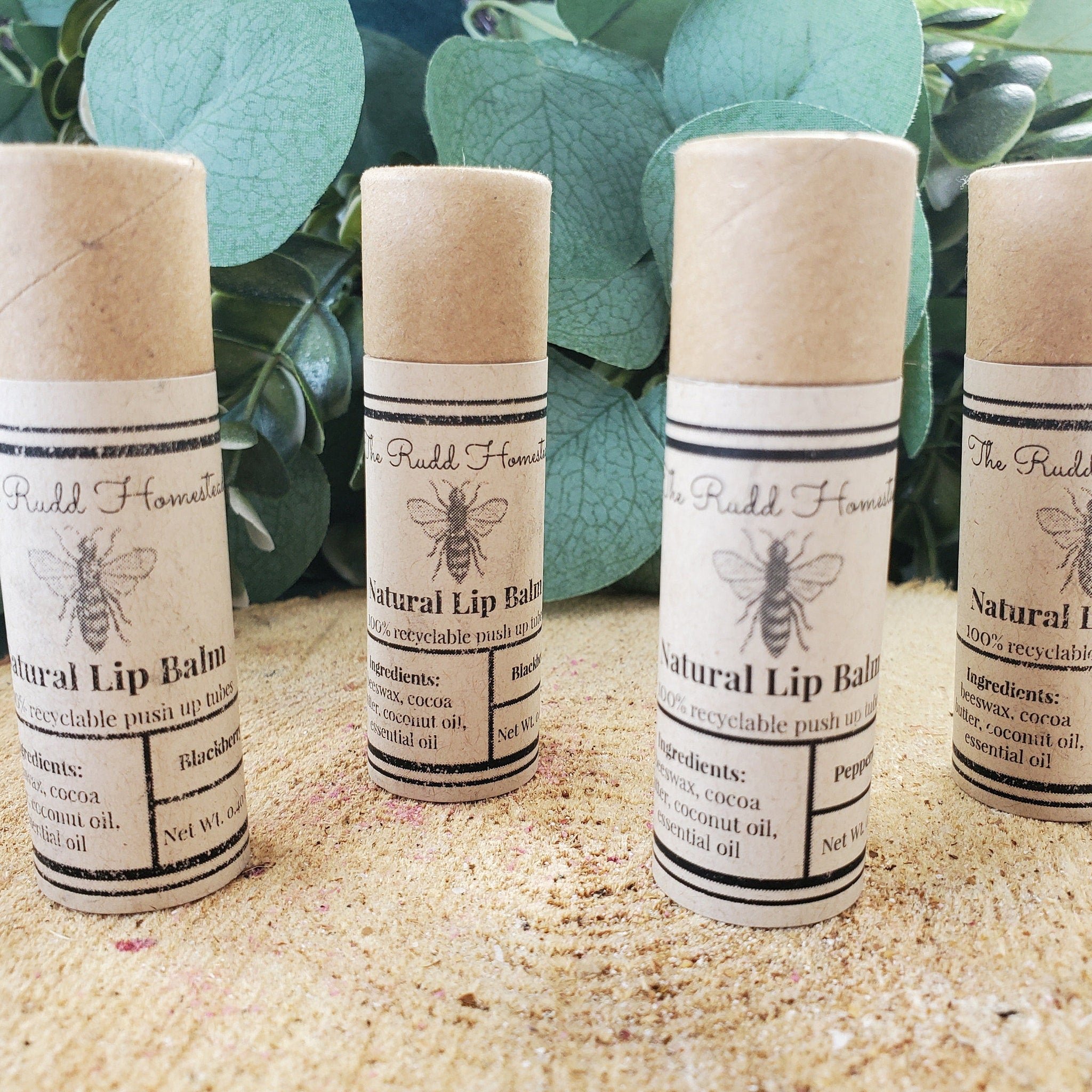 Natural lip balm tubes with brown paper, black text, and Rudd Homestead logo on display