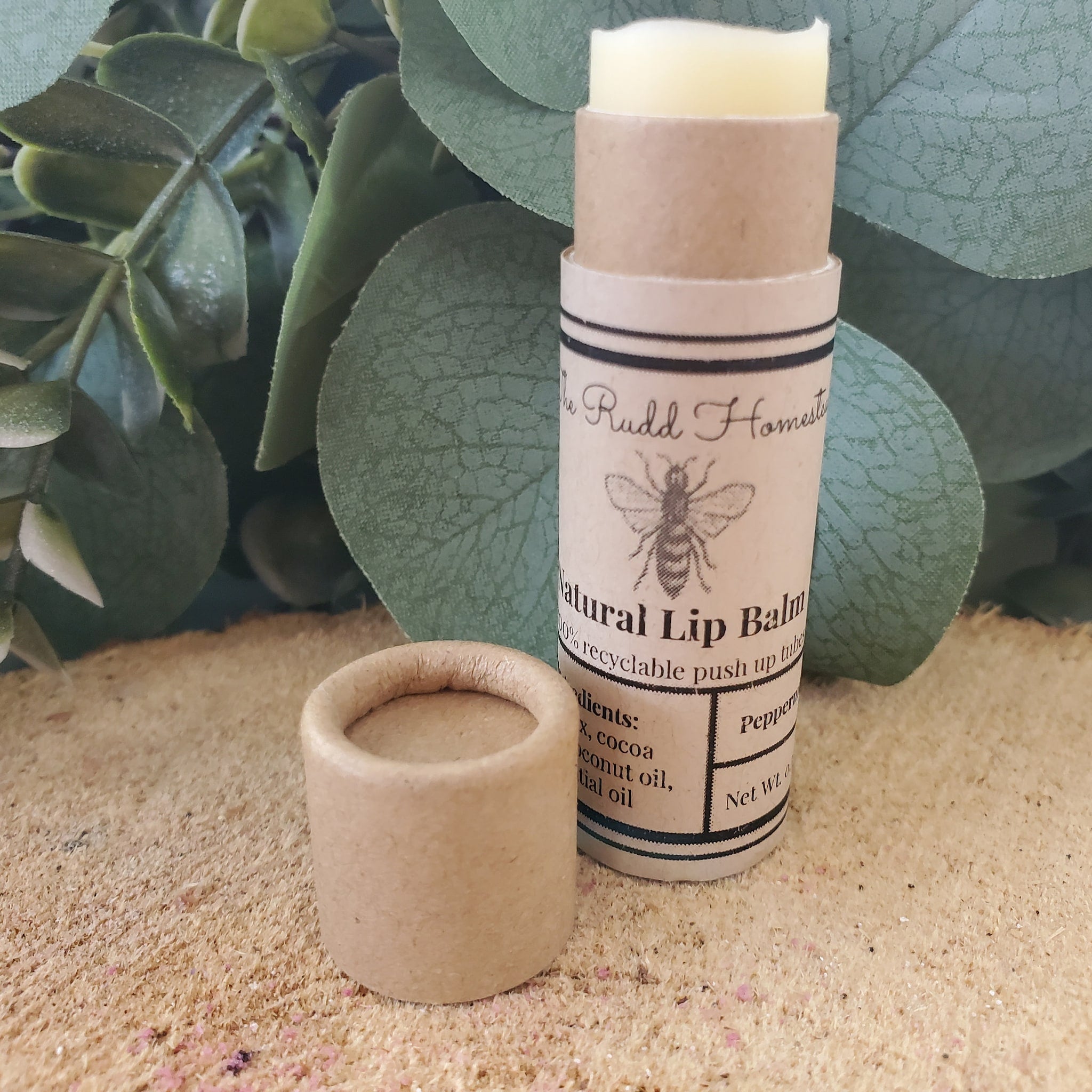 Lip balm in a tan cardboard tube with Rudd Homestead branding and a light yellow balm