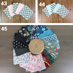 Stacked bamboo and cotton makeup remover wipes in assorted sizes with a beige pouch, laid flat on a wooden surface