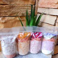 Bath salts in clear plastic bags with various colors and floral elements, displayed together