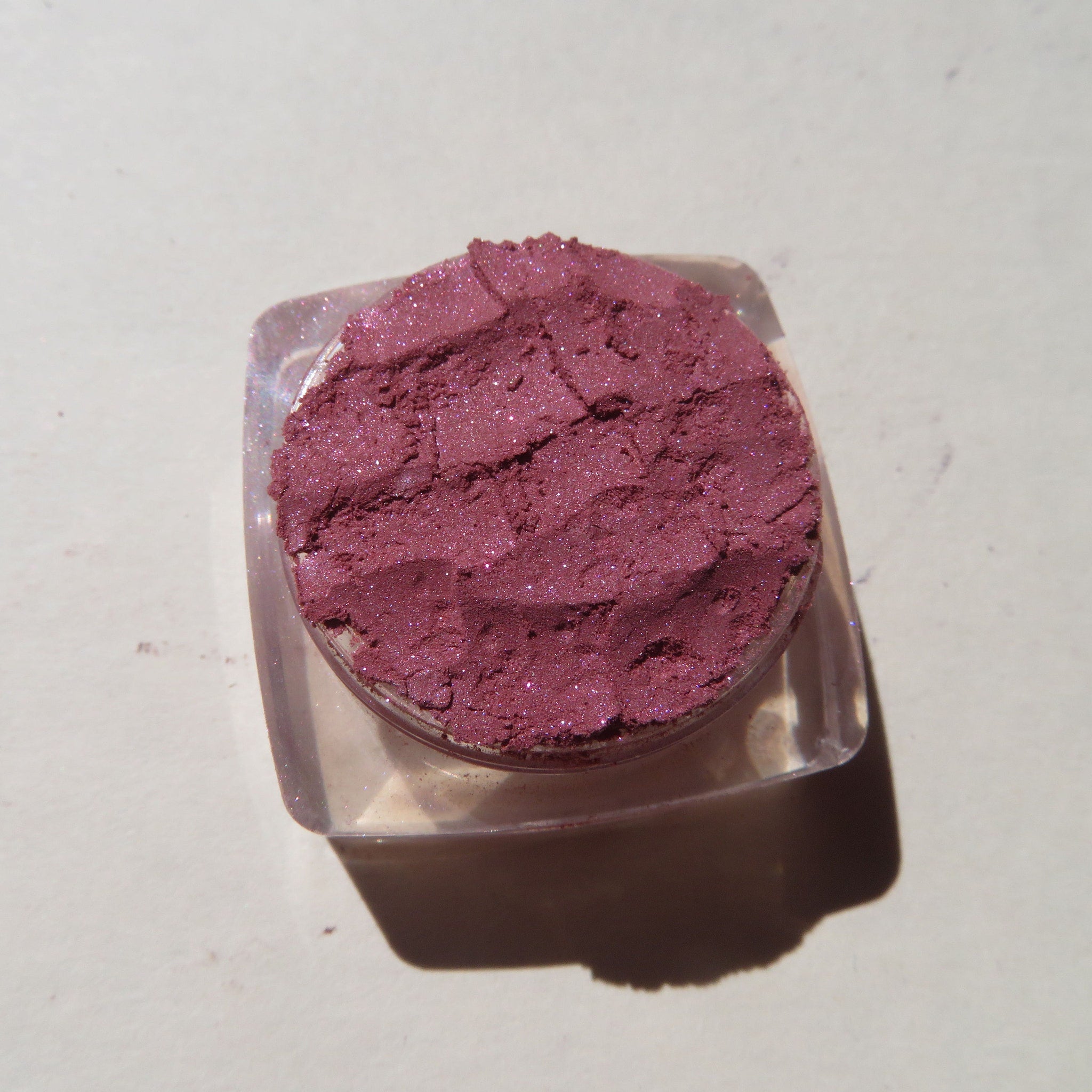 Open compact showing loose dark pink shimmer mineral eyeshadow with vegan cruelty-free label visible