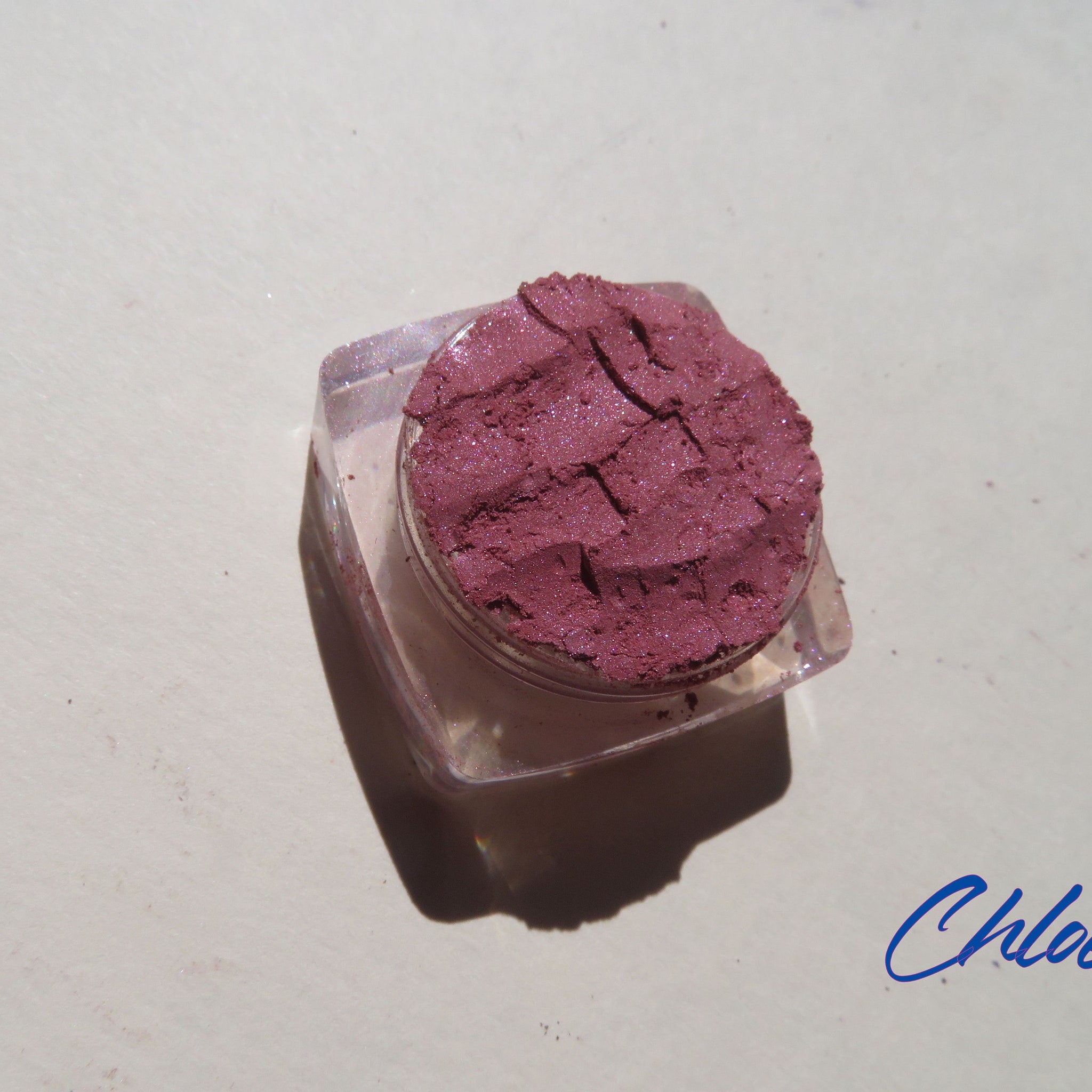 Close-up of CHLOE Vegan Mineral Eyeshadow in dark pink shimmer, loose powder with cruelty-free label, showcasing sparkly texture.