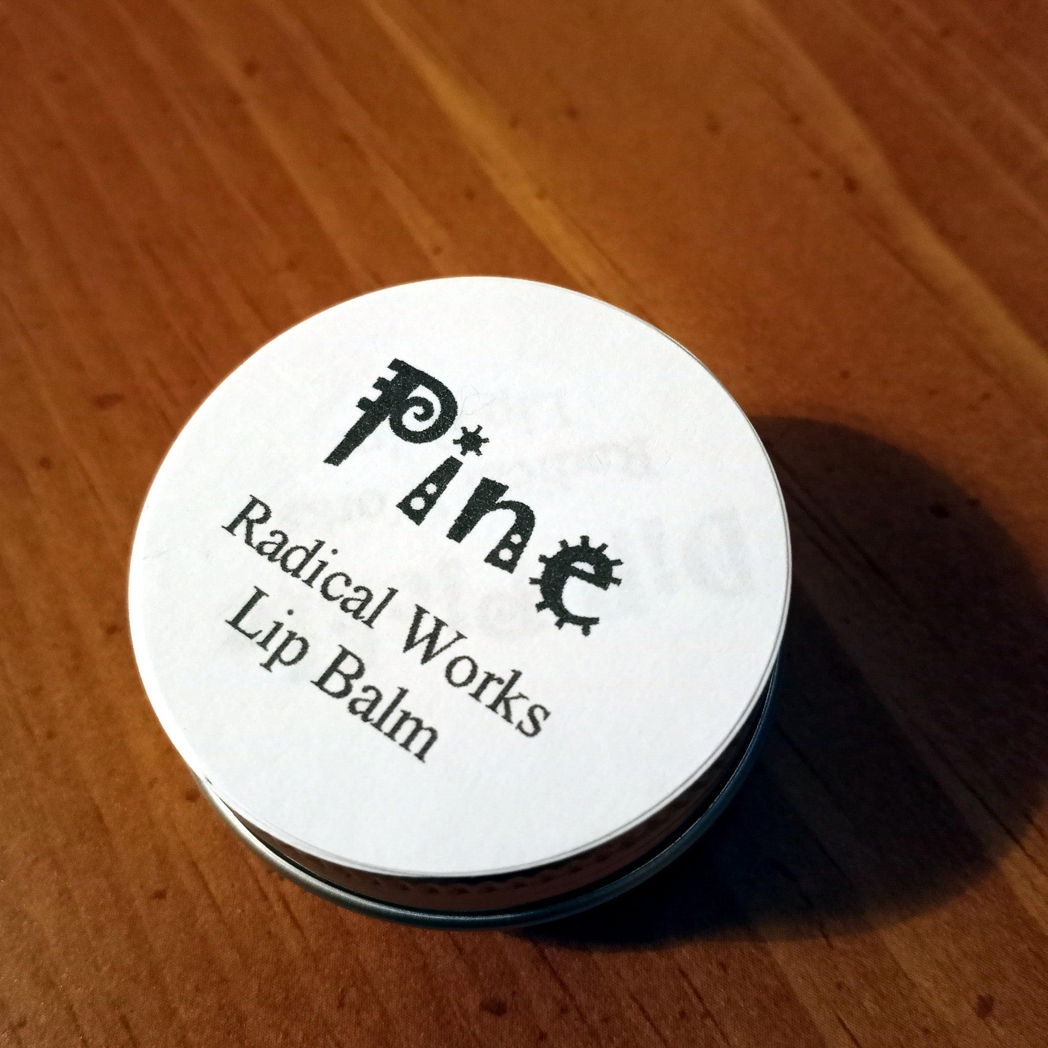 Lip balm in a round metal tin with white label, black text, and Radical Works branding