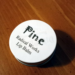Lip balm in a round metal tin with white label, black text, and Radical Works branding