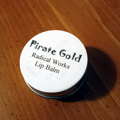 Lip balm tin with white label, black text, and Radical Works brand on wood surface
