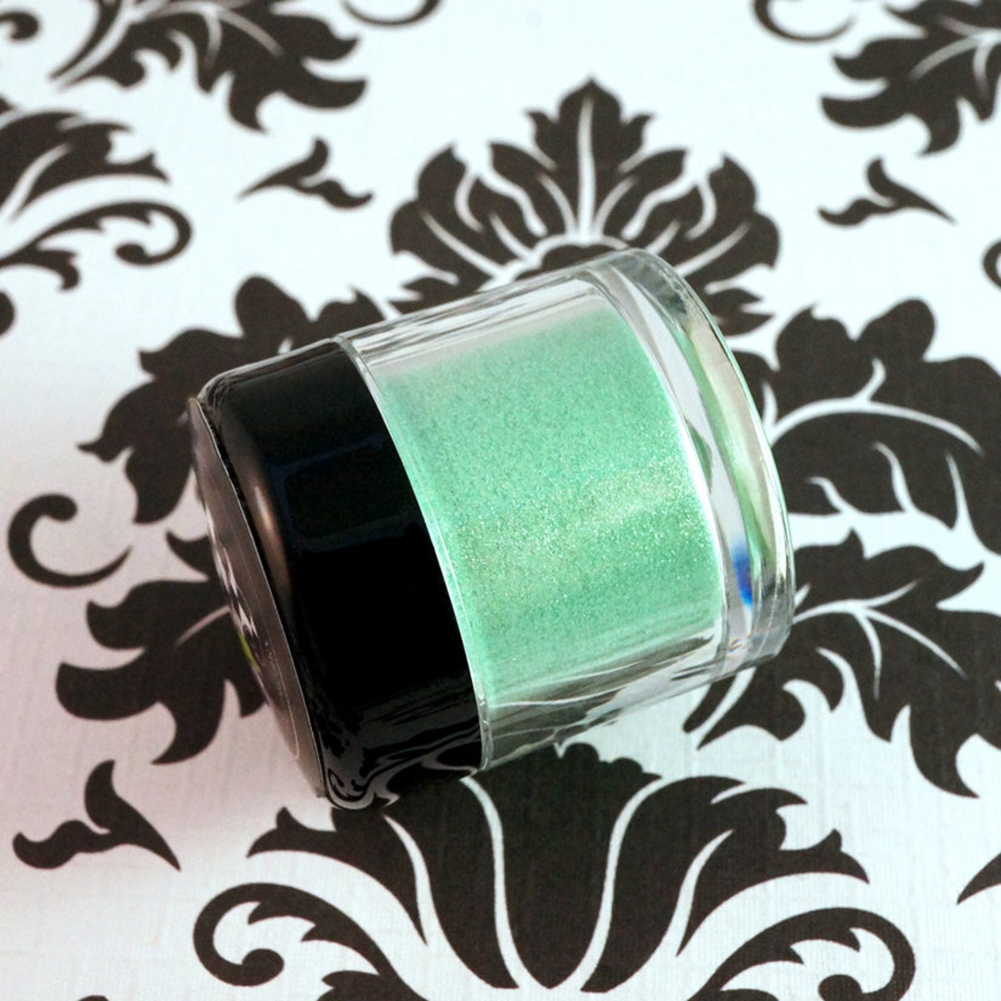 Side view of loose iridescent lime green eyeshadow pigment sparkling in metallic candy apple tones
