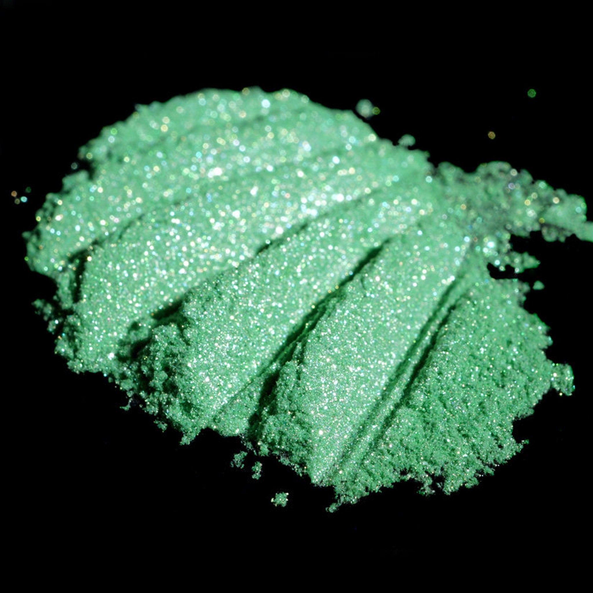 Side view of loose iridescent lime green eyeshadow pigment shimmering with metallic candy apple flecks in jar