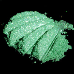 Side view of loose iridescent lime green eyeshadow pigment shimmering with metallic candy apple flecks in jar