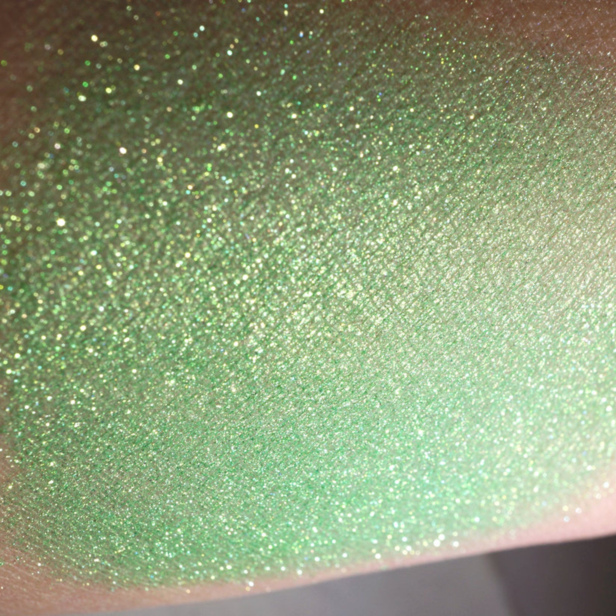 Close-up of loose iridescent lime green eyeshadow pigment with metallic candy apple sheen