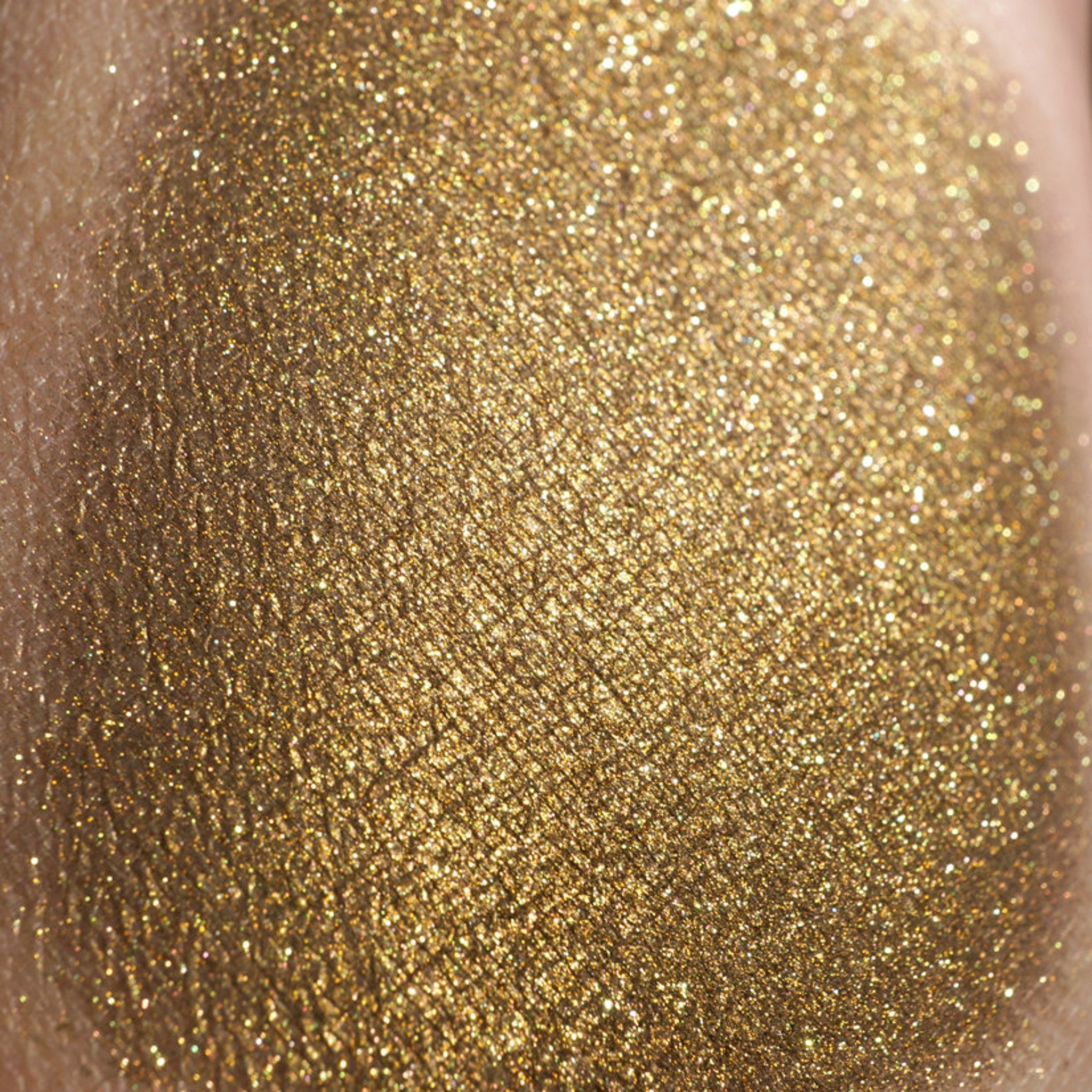 Close-up of loose dark gold eyeshadow with green glitter sparkles in metallic bronze packaging
