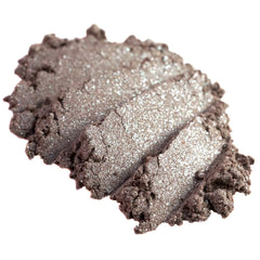 Close-up of loose metallic taupe and champagne eyeshadow pigment with silver shimmer particles scattered on skin