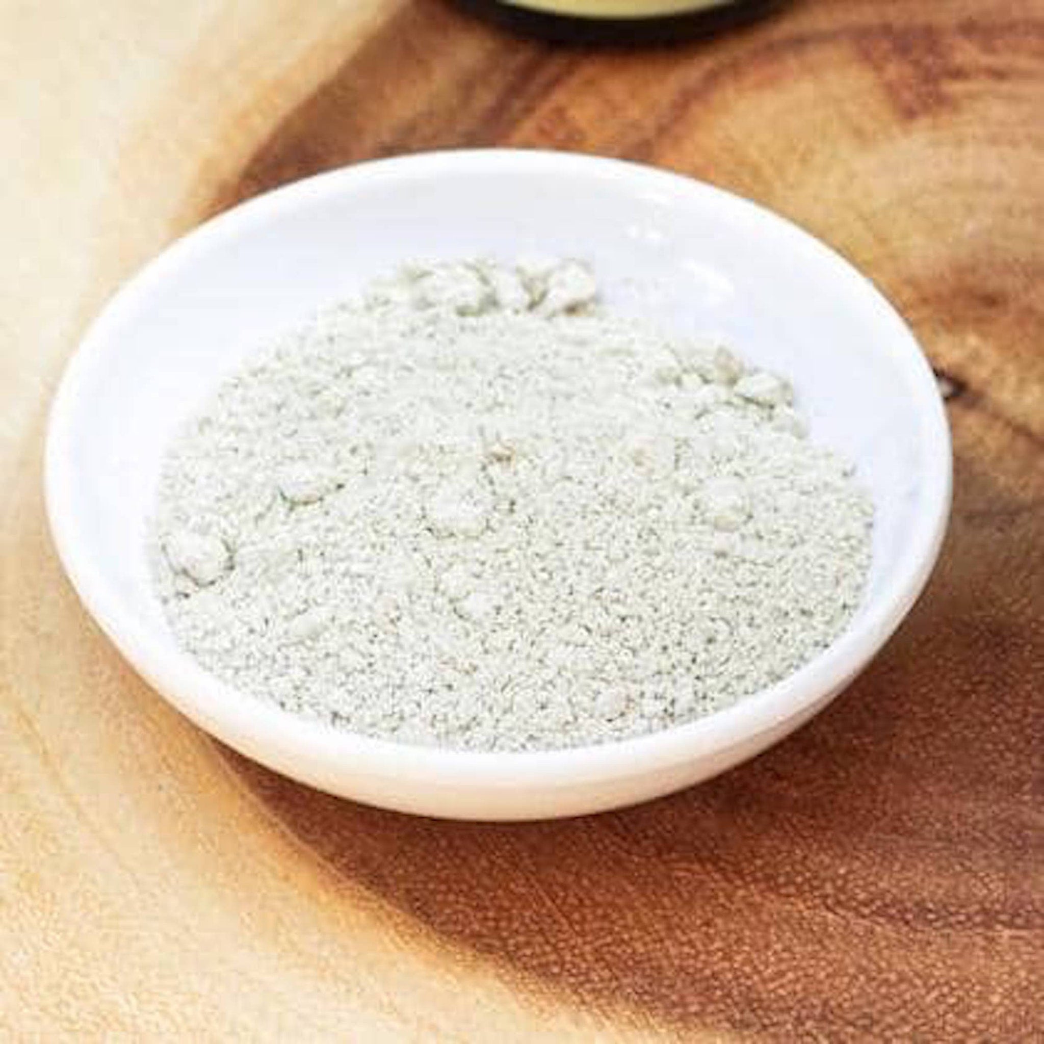 Powdered product in white ceramic bowl, light green granules, on wooden surface