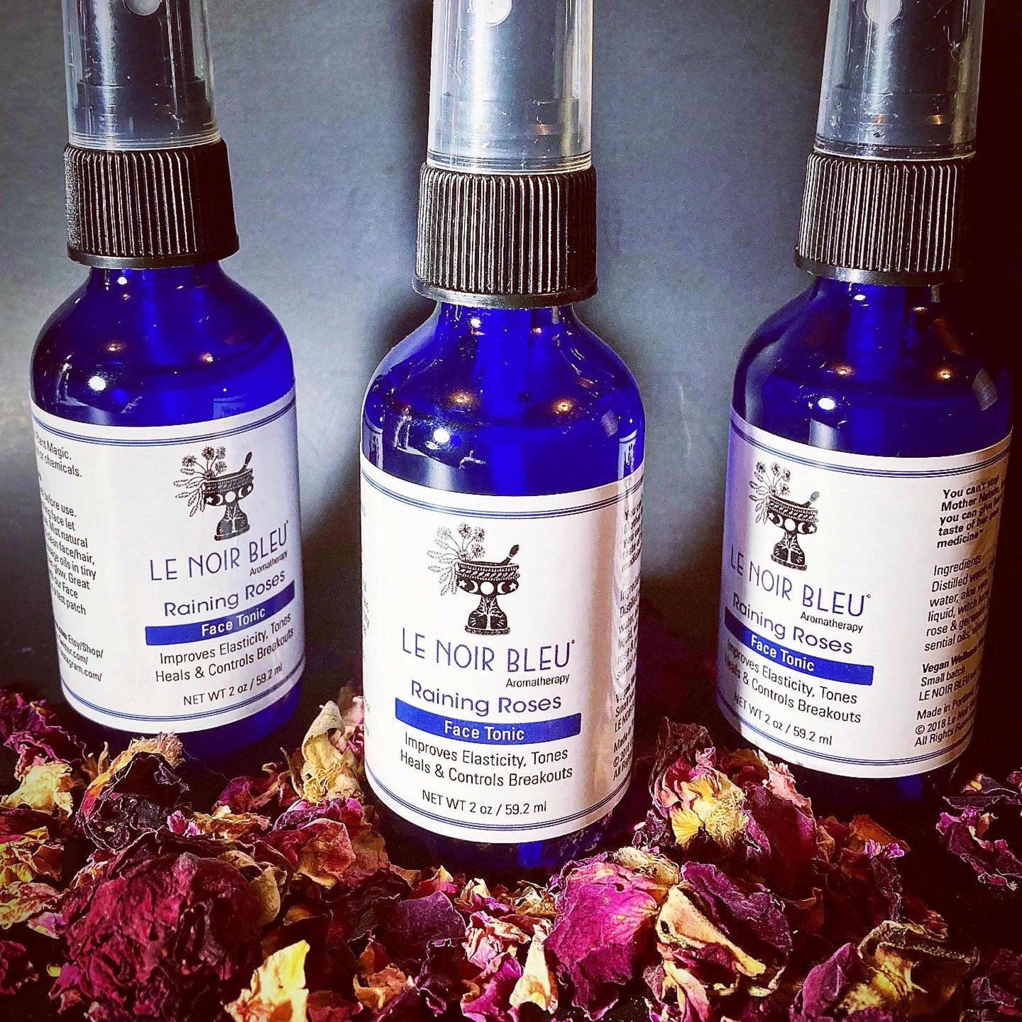 Face tonic bottles with blue glass, black cap, and white label, surrounded by rose petals