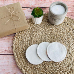 White reusable facial pads on woven mat with candle and gift box