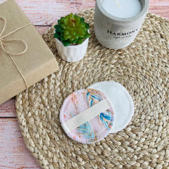 Reusable makeup pads with pink feather pattern, white terrycloth, and elastic band on woven mat