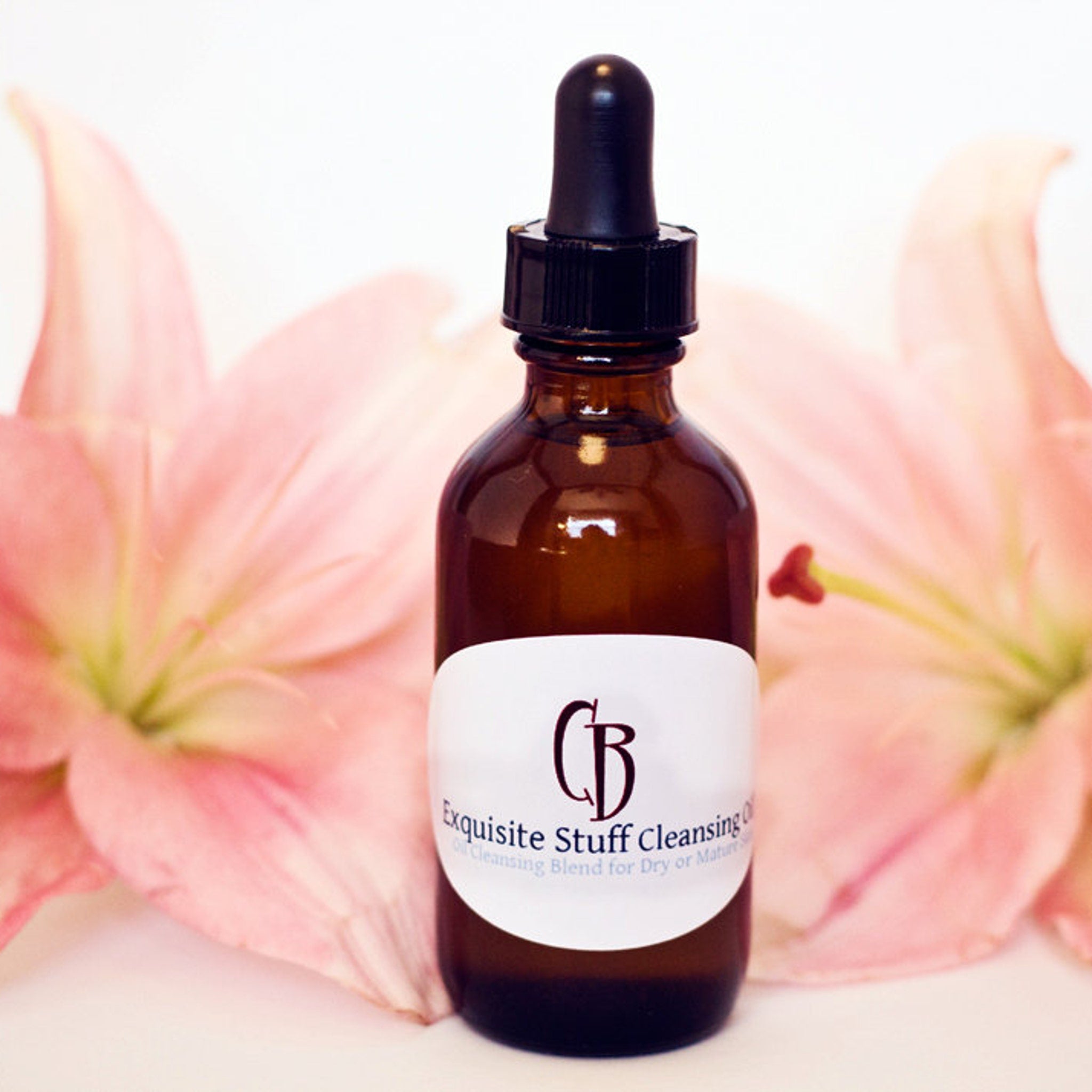 Facial cleanser brown glass bottle with black dropper, white label, and pink flower background