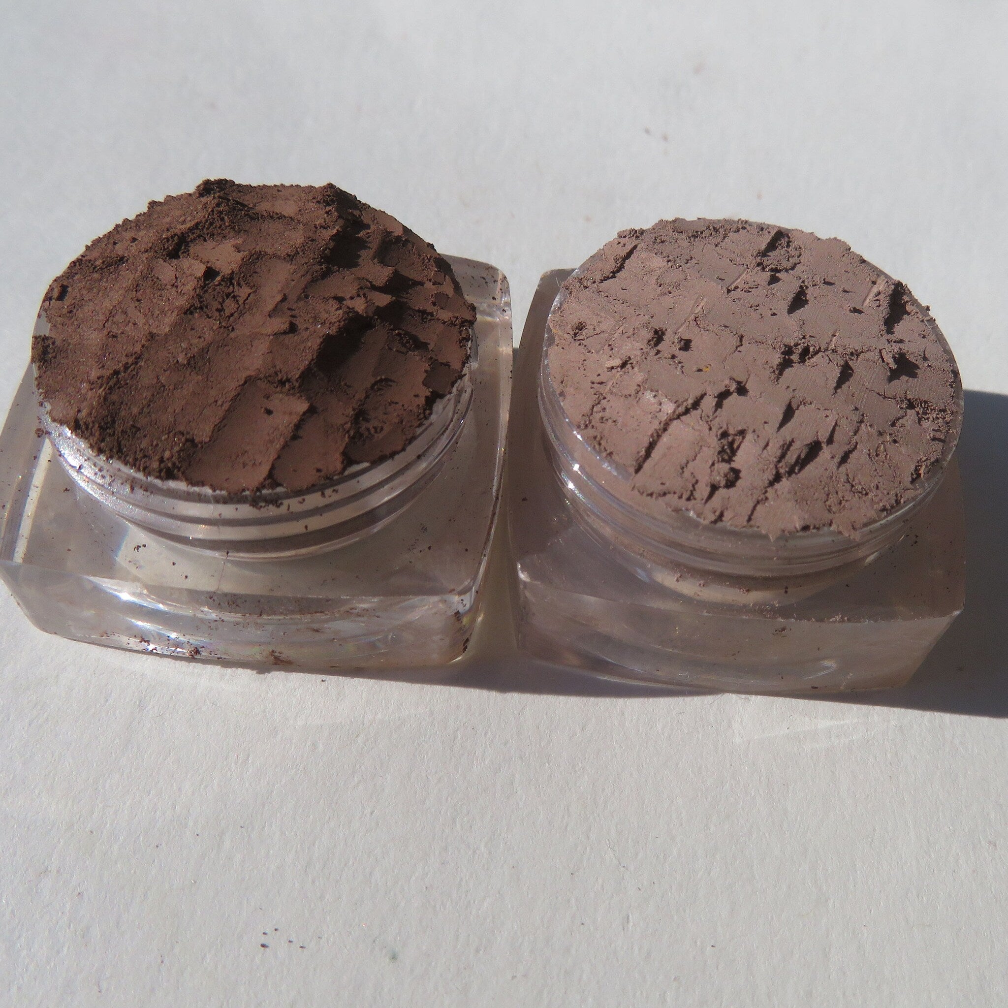 Side view of three matte brown loose pigment eyeshadows in sleek round jars with black lids