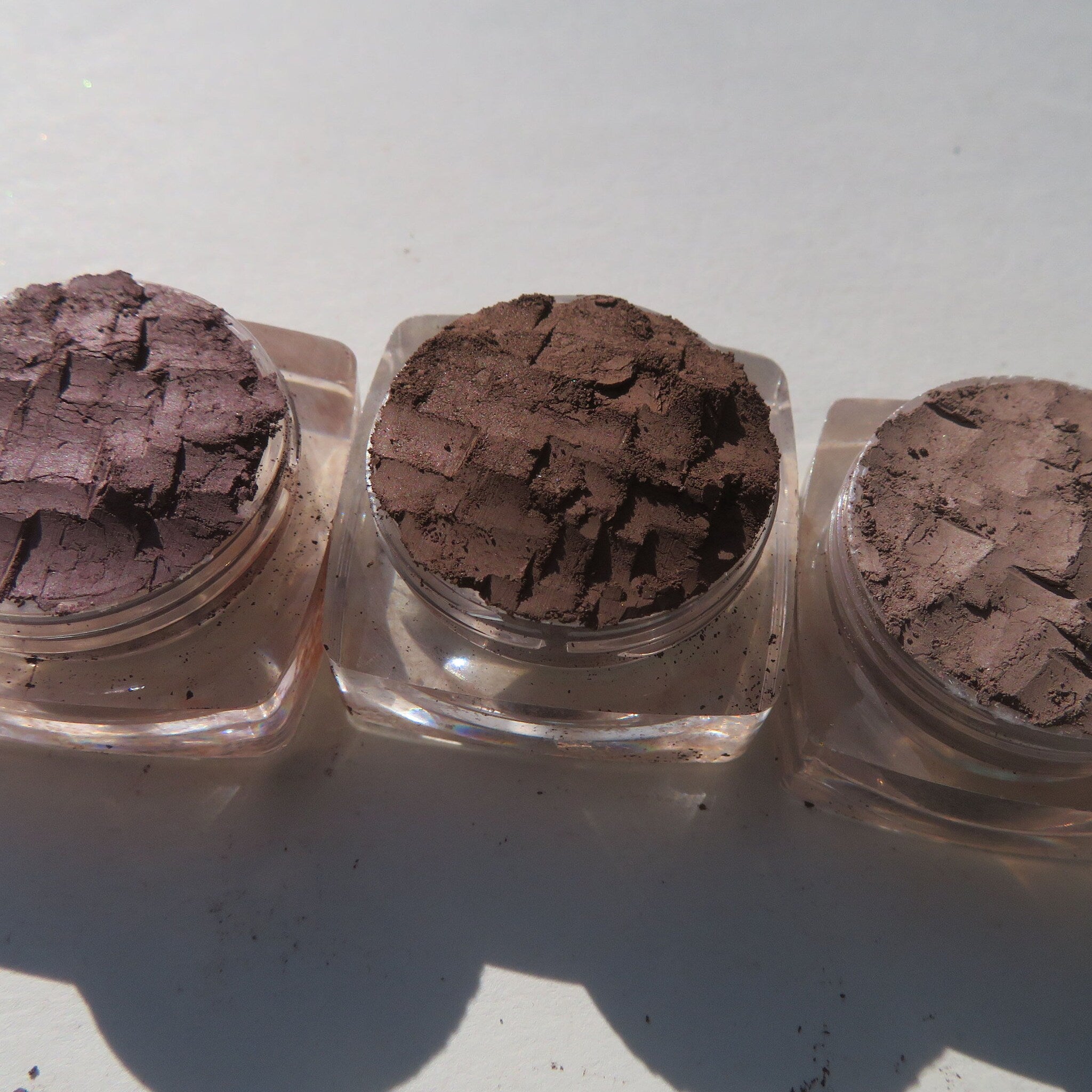 Side view of three matte brown loose pigment eyeshadows in sleek cylindrical jars with black lids