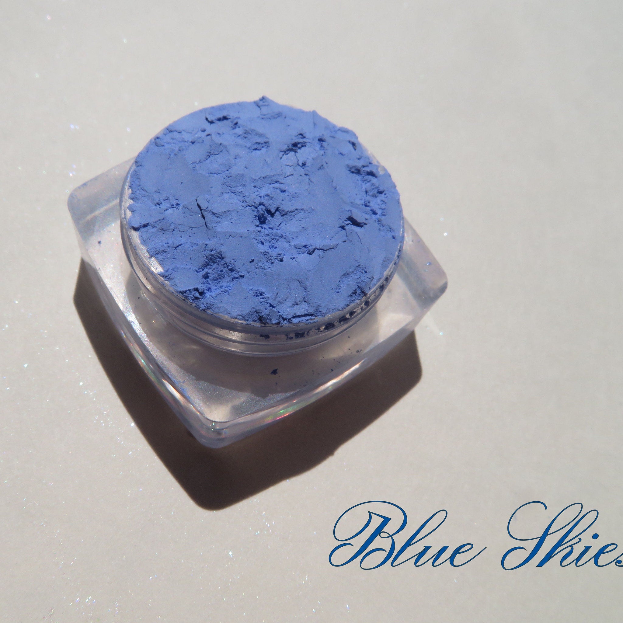 Close-up of matte sky blue mineral eyeshadow in a clear jar with black screw-top lid and silver label.