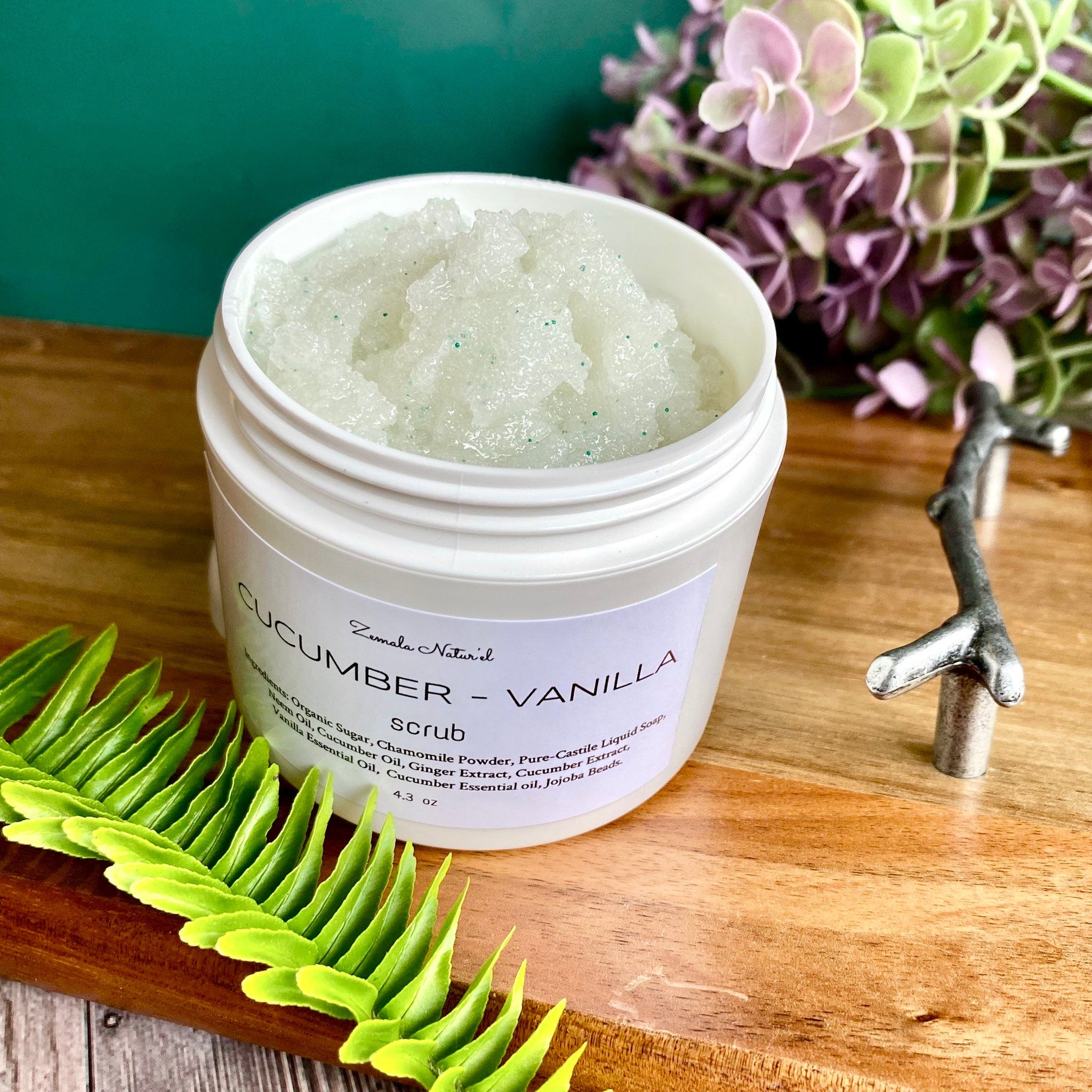 Body scrub in white jar with green flecks, Zemala Naturel label, on wood surface