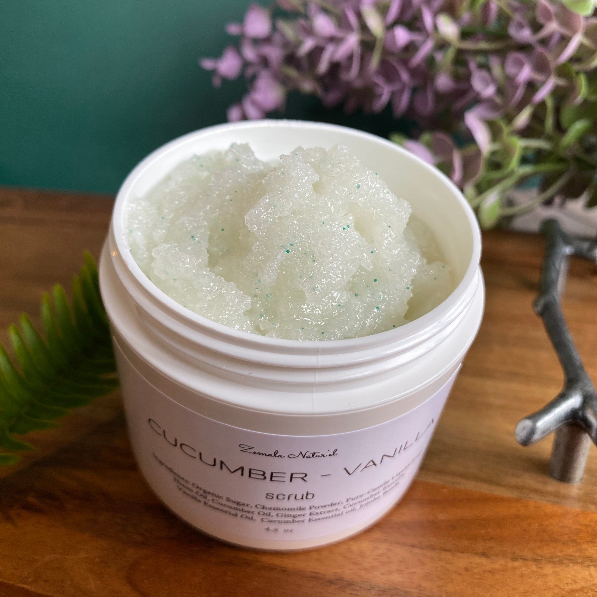Body scrub in white jar with green granules, Zemala Naturel Cucumber Vanilla visible on label, on wood surface