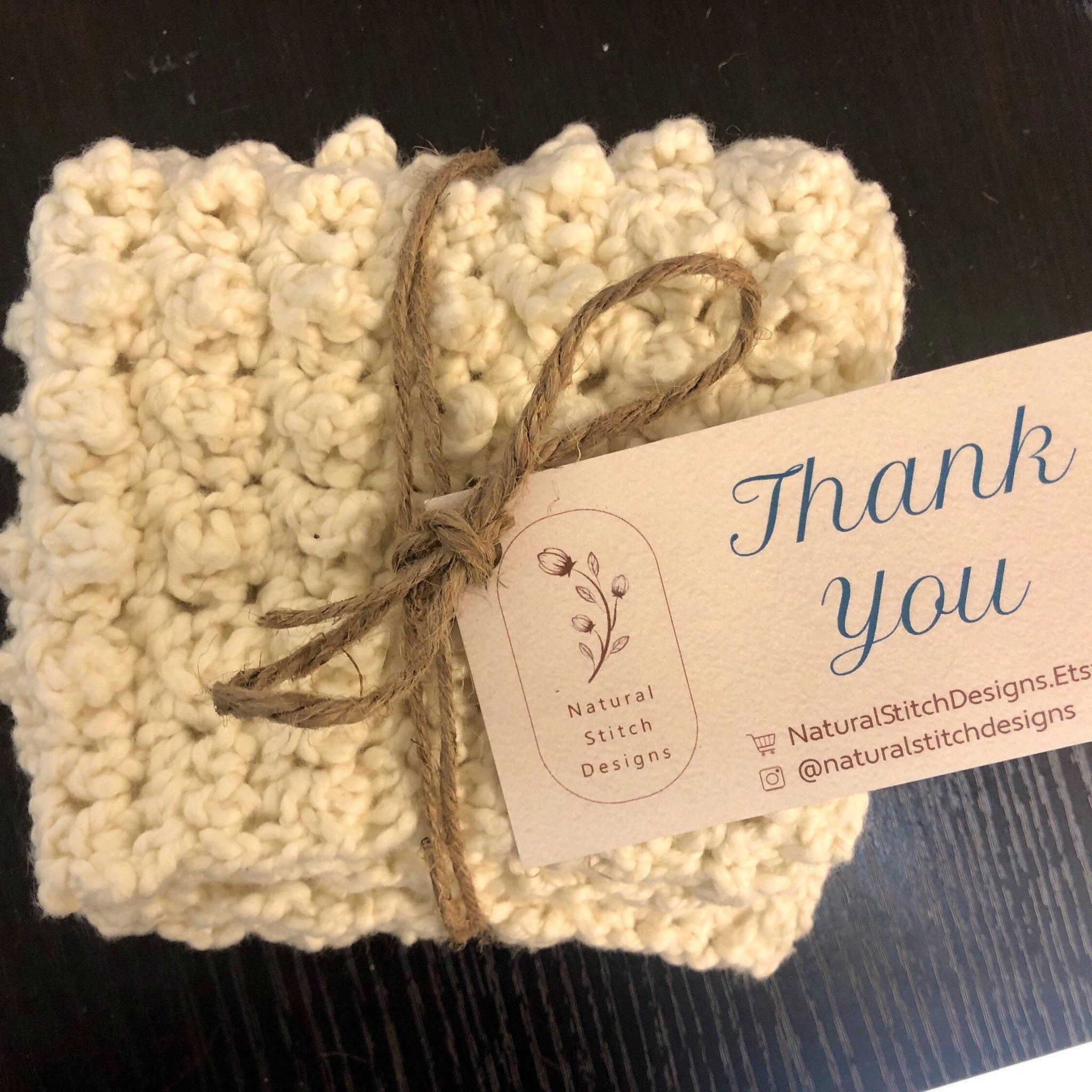 Cream-colored crocheted washcloths tied with twine, Natural Stitch Designs branding visible on tag