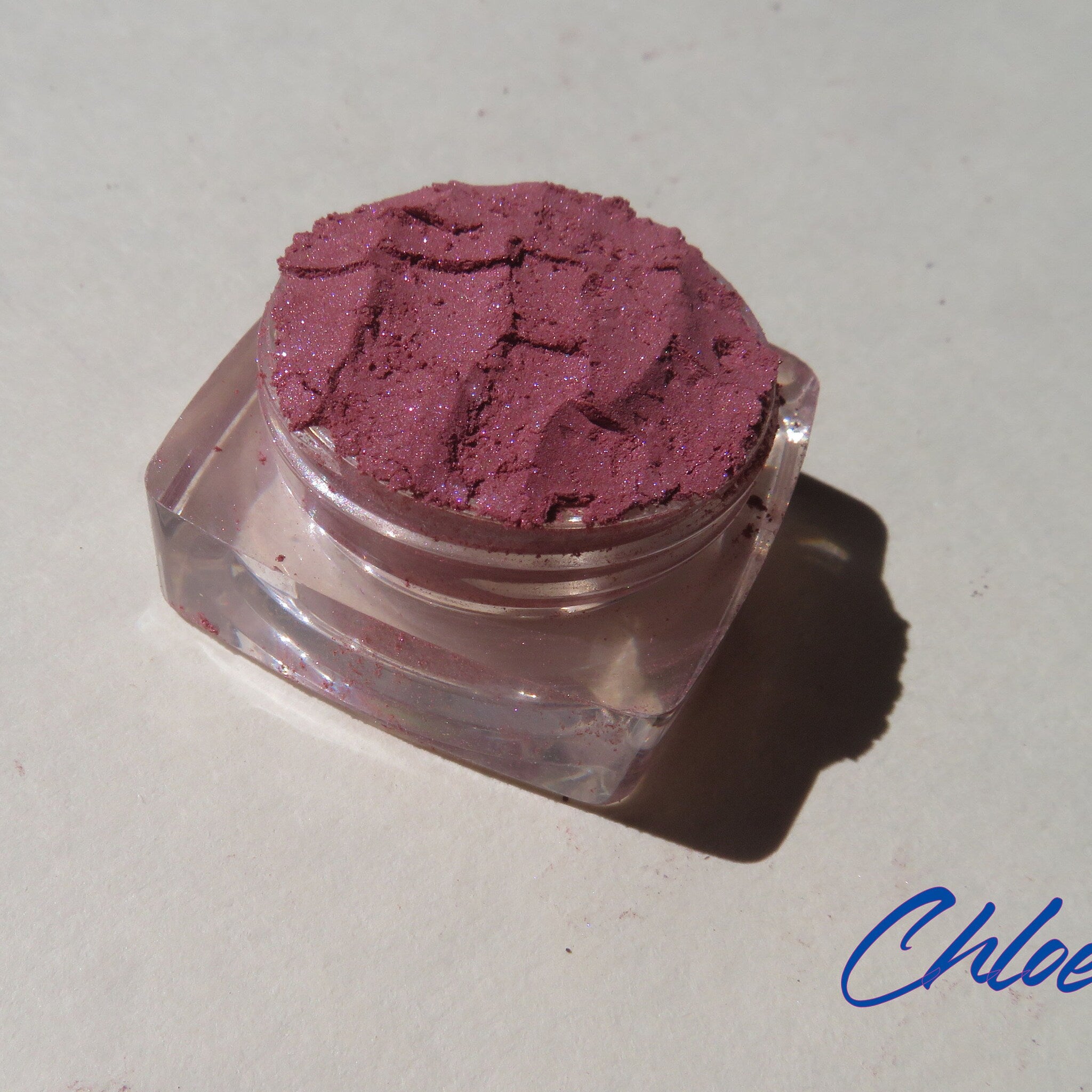 Close-up of loose dark pink shimmer eyeshadow powder with vegan mineral particles in a compact container