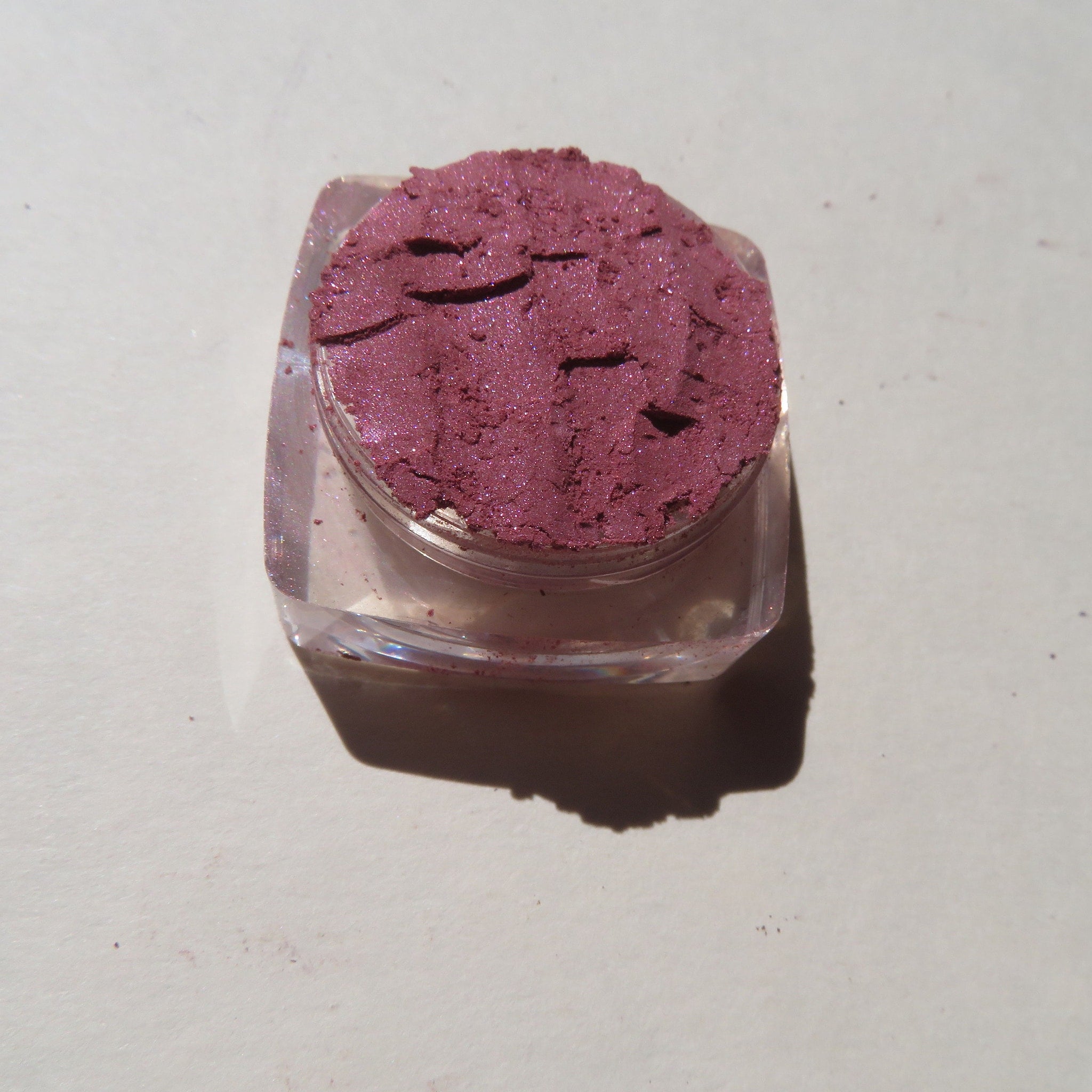 Eye shadow, shimmering mauve powder in clear plastic container, close-up shot