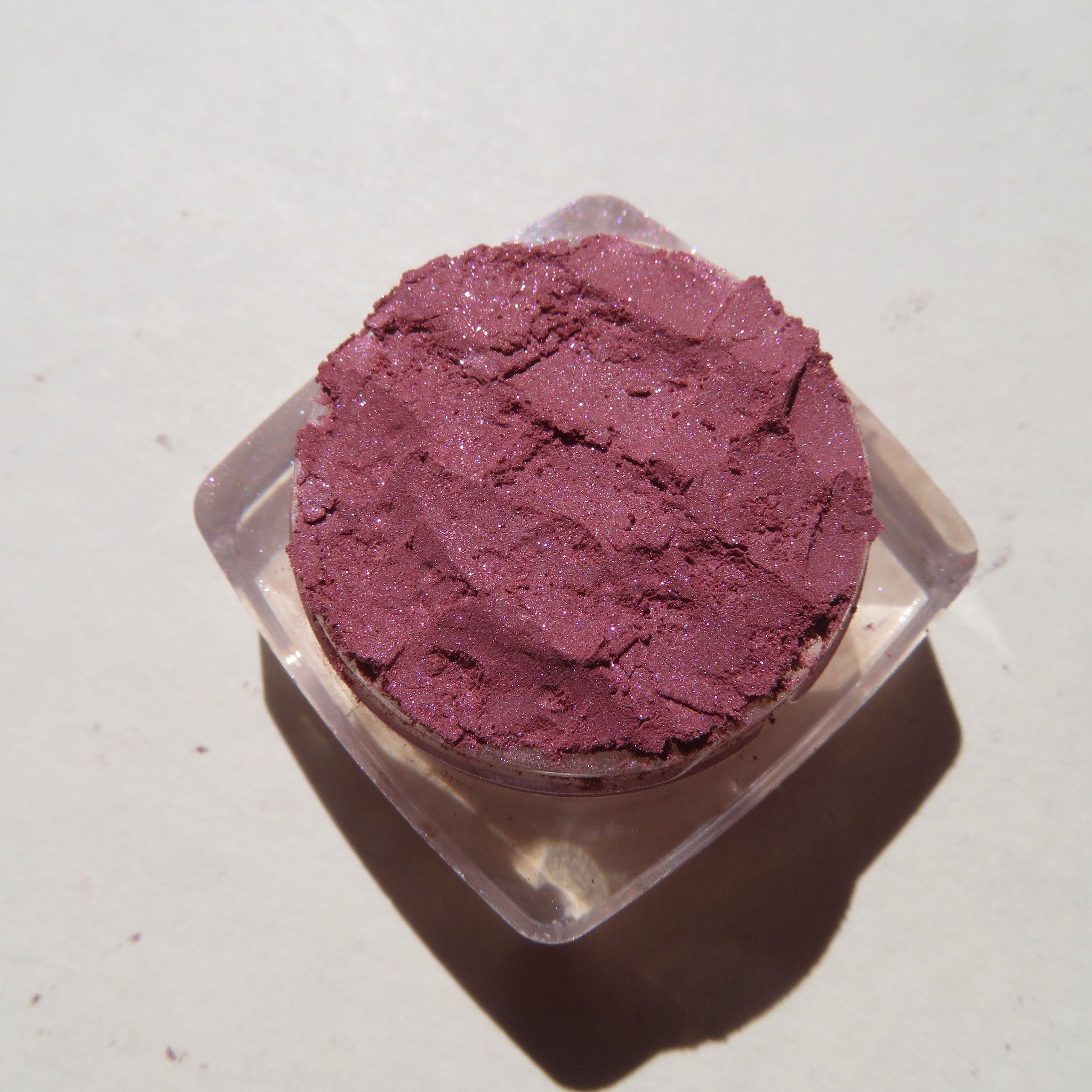 Eye shadow powder in burgundy with glitter, in a clear plastic container, top view