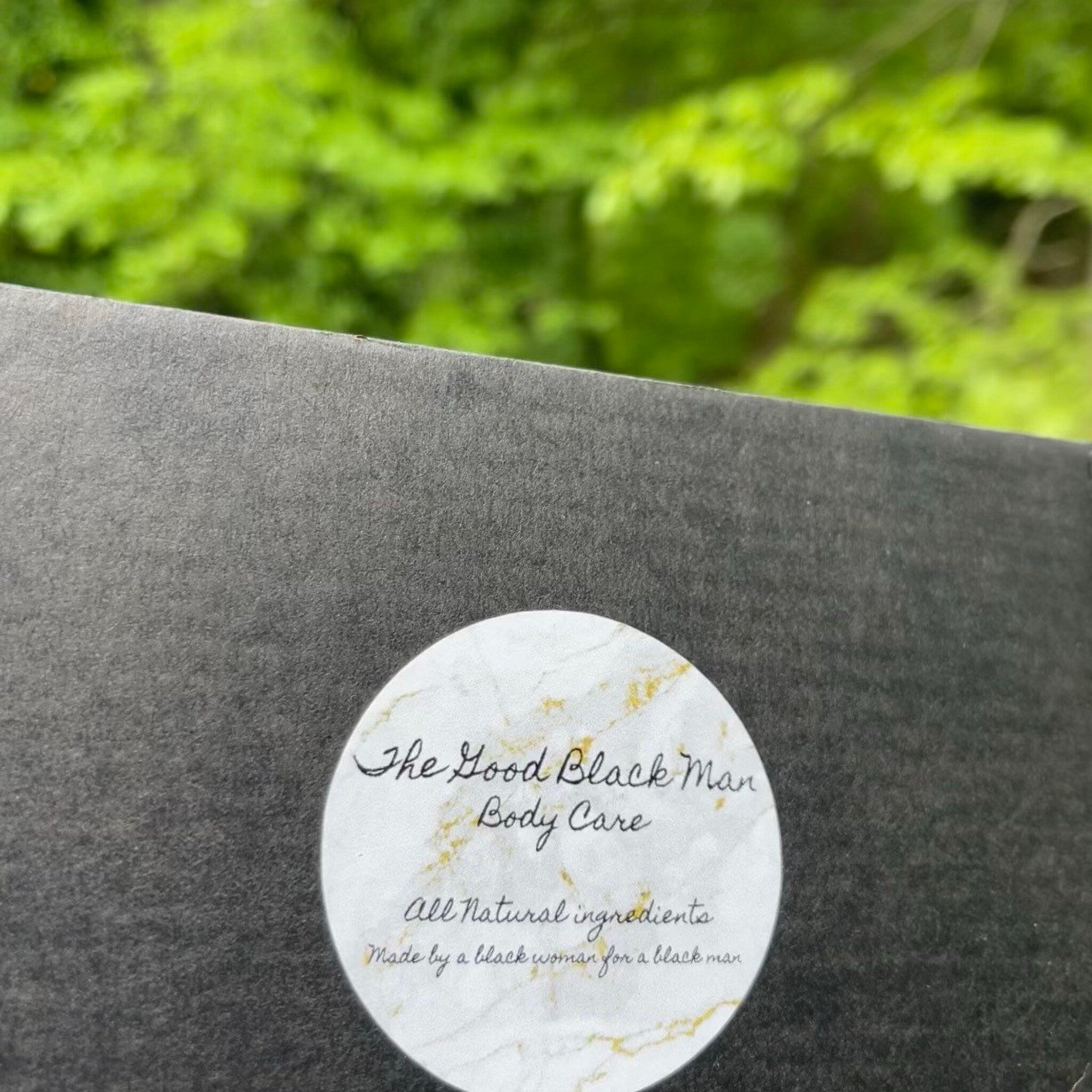 Body care product, dark gray box, white label with gold accents, "The Good Black Man" text
