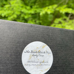 Body care product, dark gray box, white label with gold accents, "The Good Black Man" text