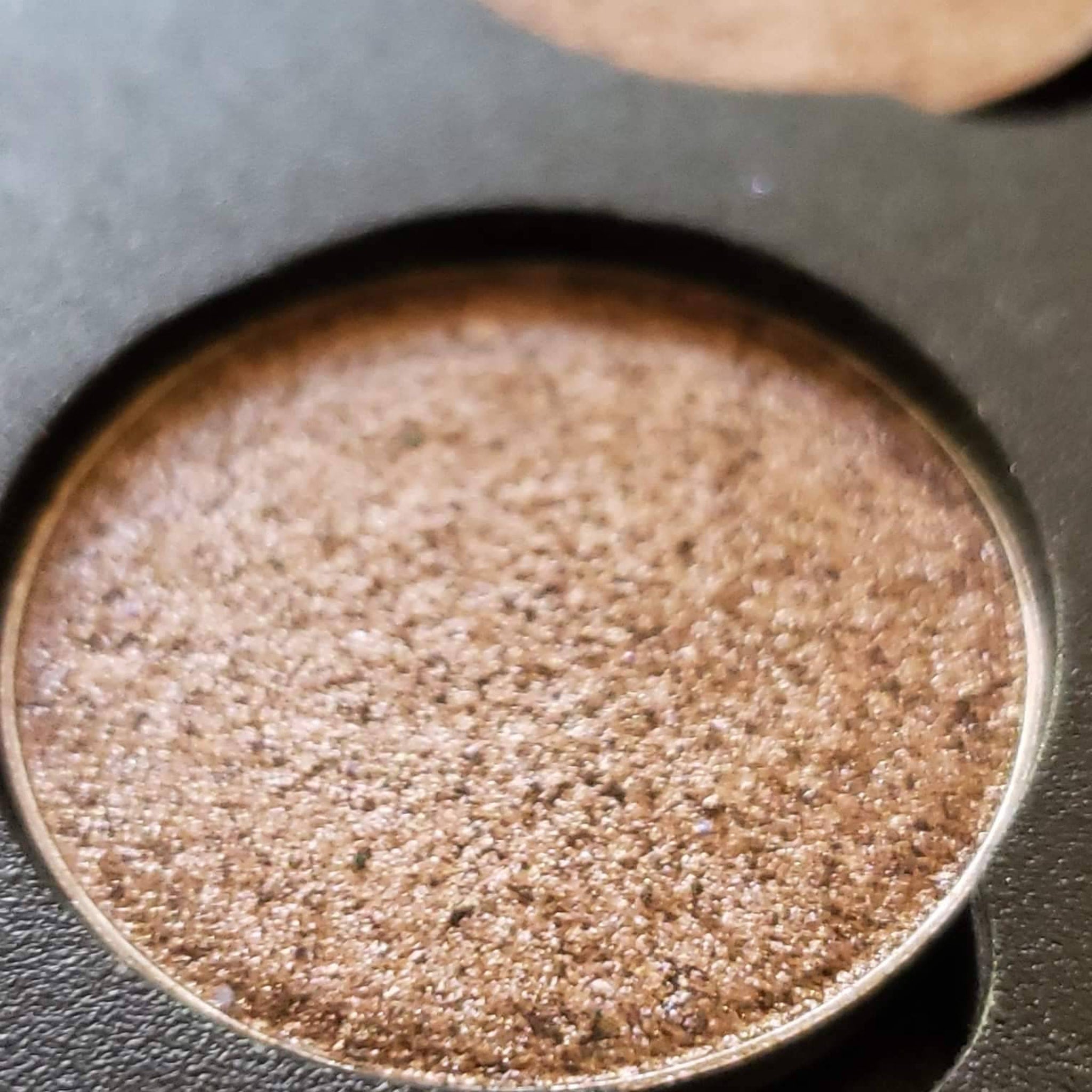 Side view of Coco Bronze Beige Brown duochrome eyeshadow pan showing metallic chromatic shift in angled lighting