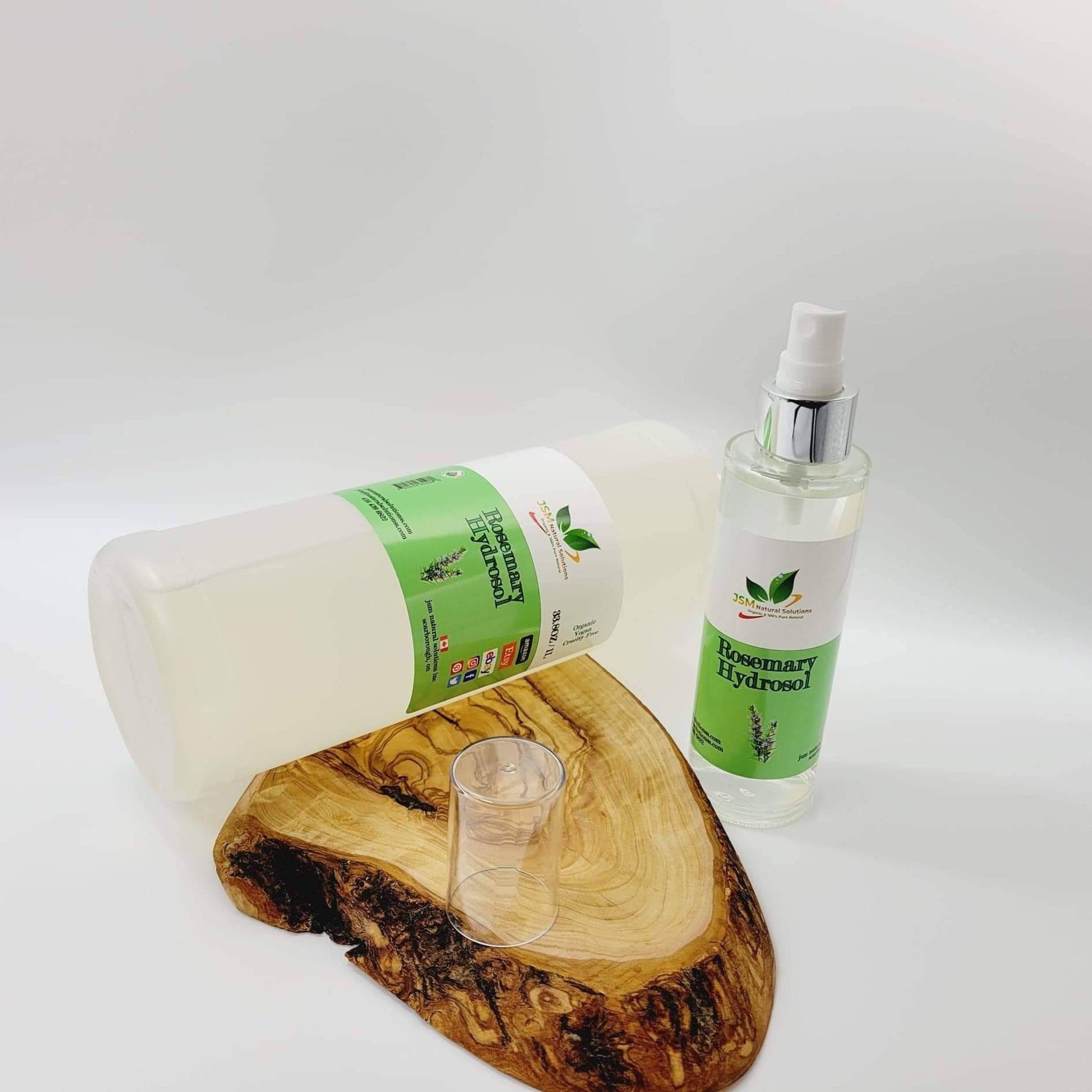 Rosemary Hydrosol bottles with green and white labels, clear liquid, and glass cup on a wooden board