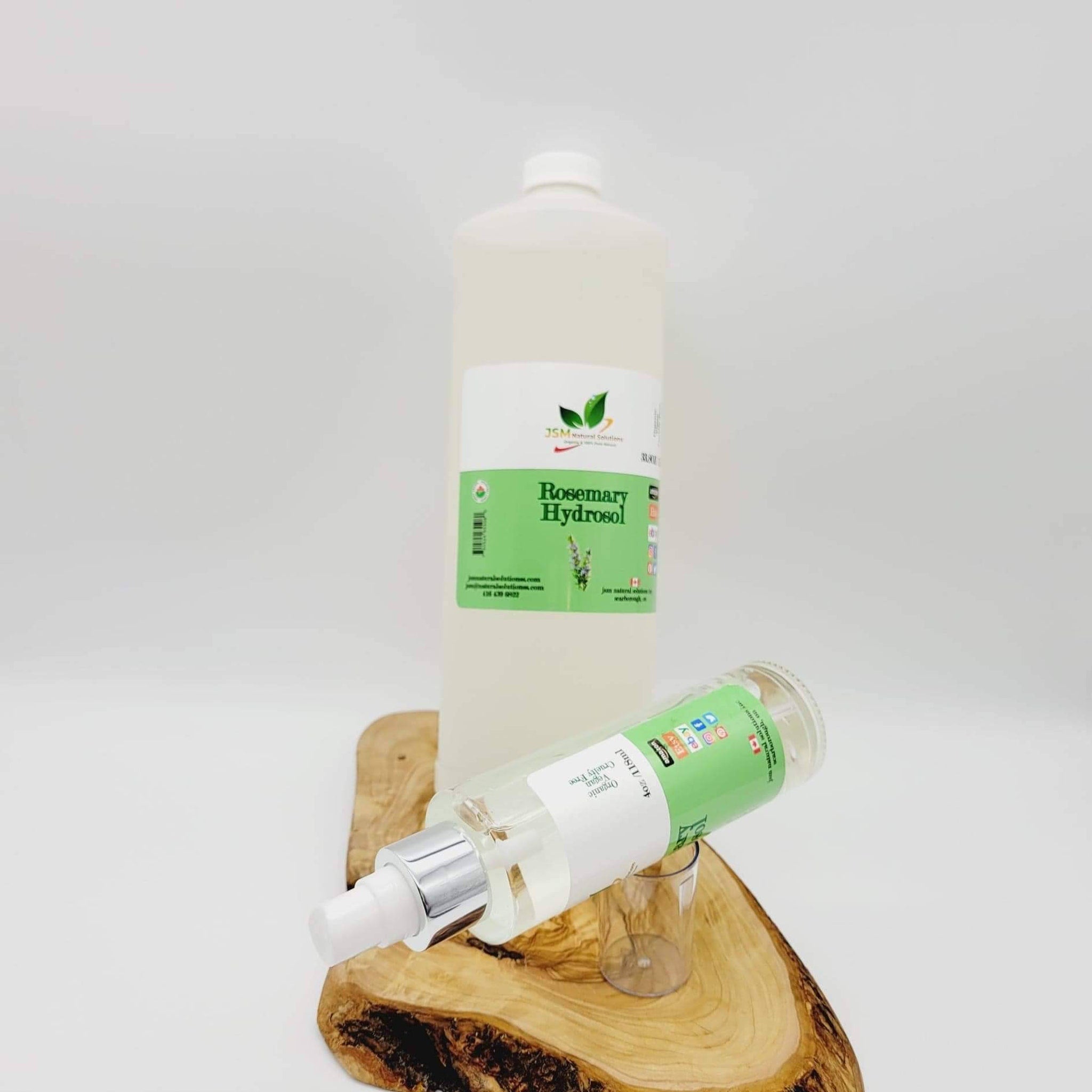 Rosemary Hydrosol bottles, clear glass, green label, silver spray top, on wood slab