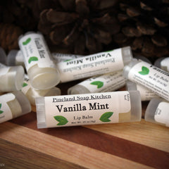 Lip balm tubes with white labels, green leaf logo, and Pineland Soap Kitchen text on wood surface