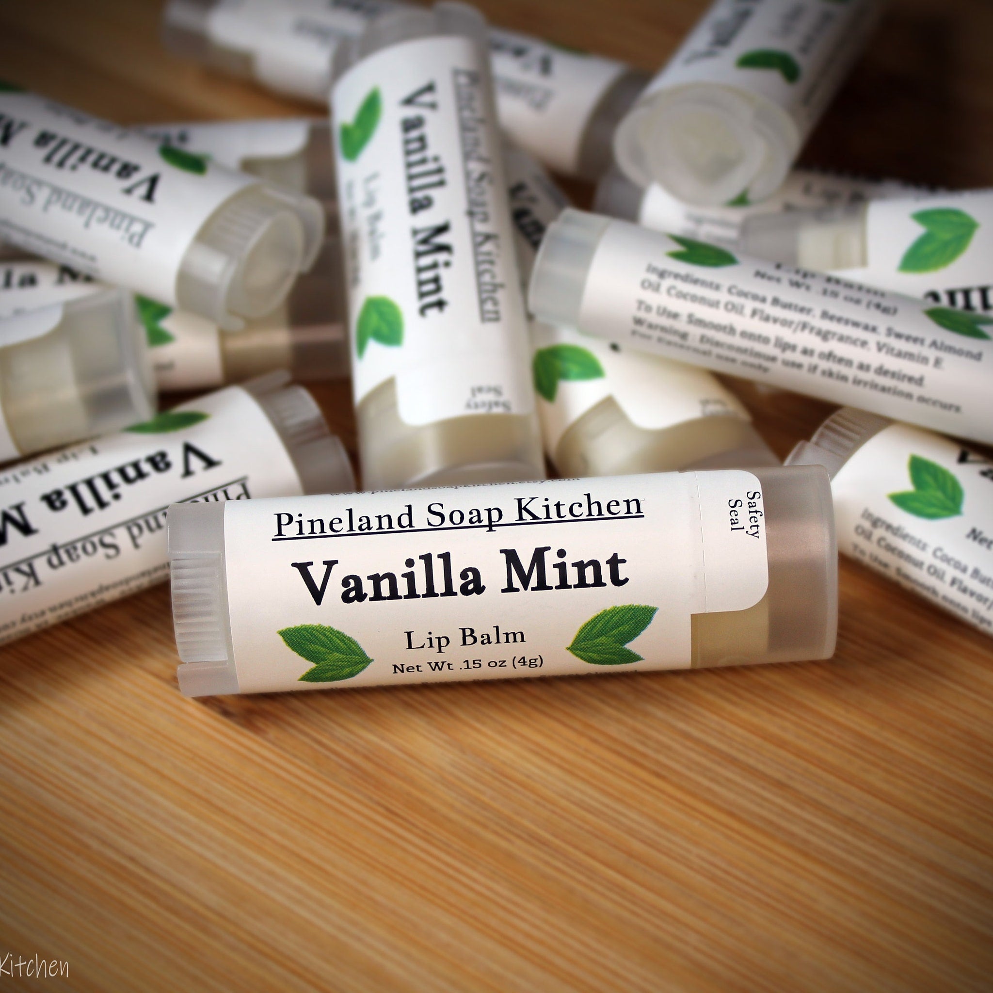 Lip balm tubes with white labels, green leaf accents, and "Vanilla Mint" text, on wooden surface