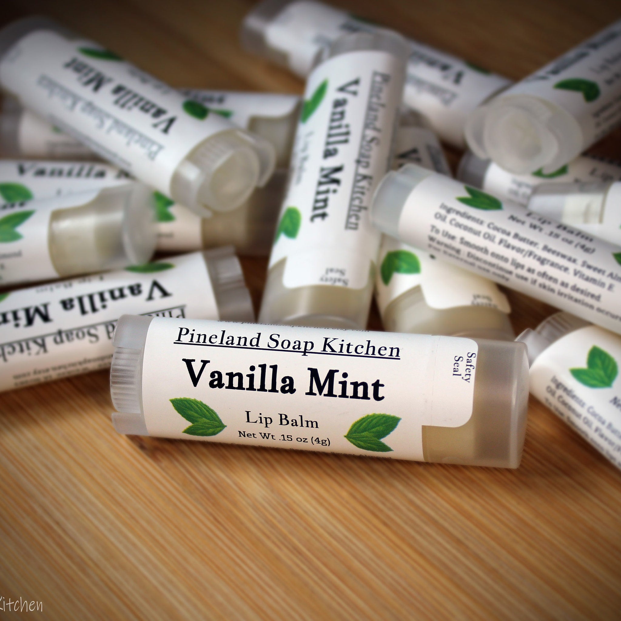 Lip balm tubes with white labels, green leaf logo, and "Vanilla Mint" text, on wooden surface