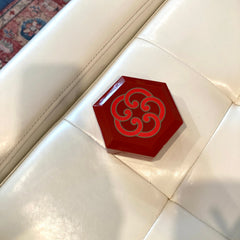 Red hexagonal decorative object with gray swirl pattern on white surface