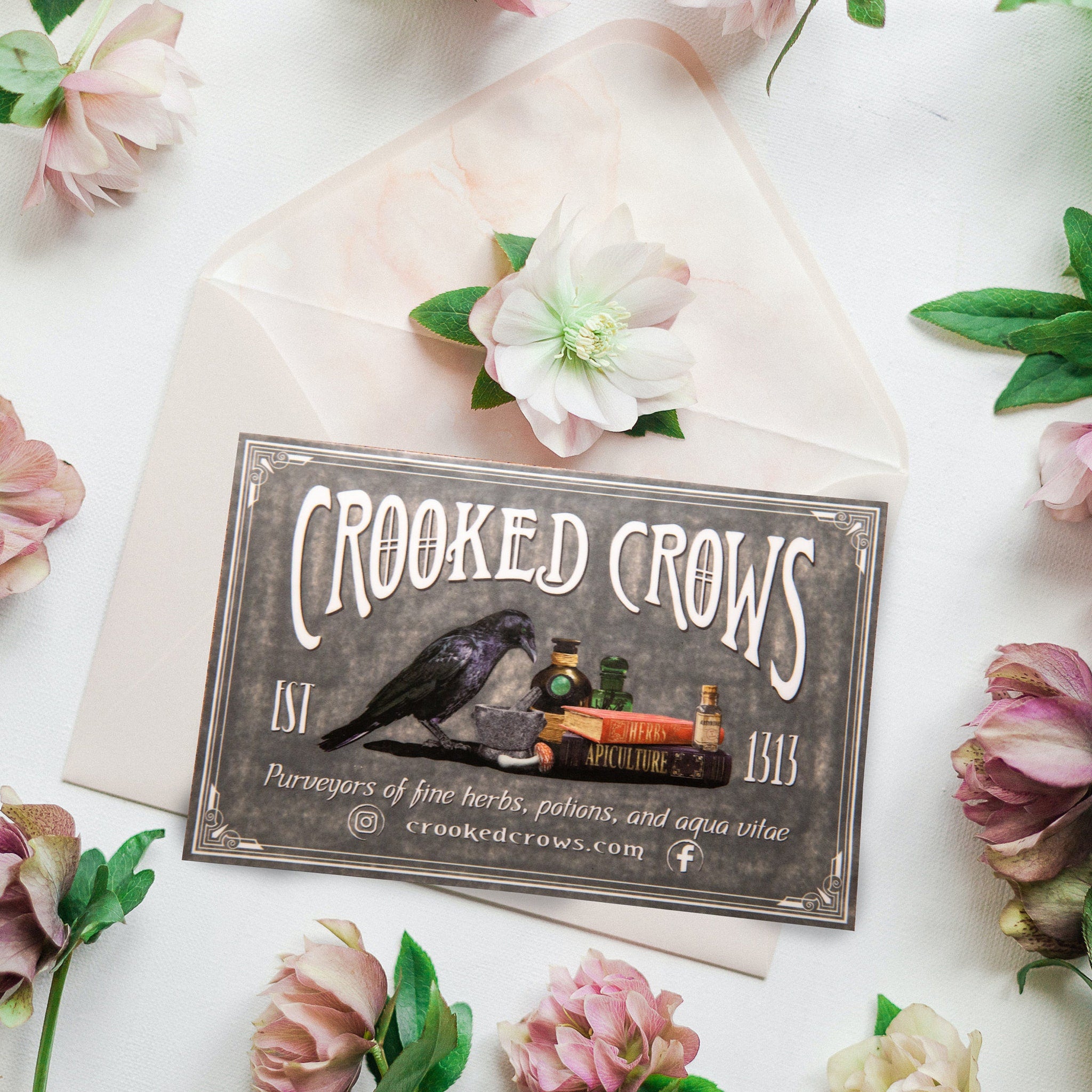 Greeting card with Crooked Crows text, dark gray with white text, surrounded by pink flowers and envelope